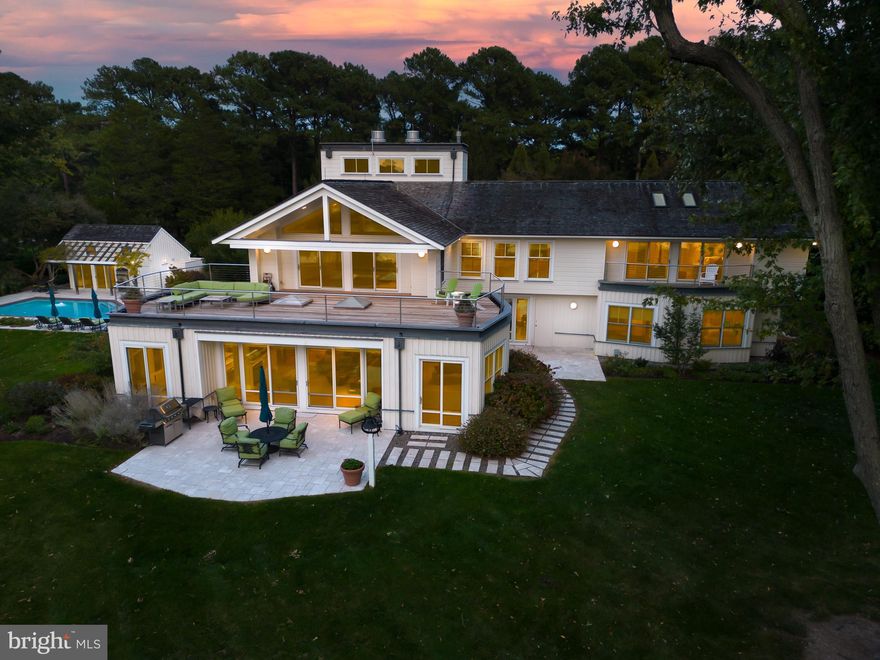 This sophisticated, elegant modern home has been designed and built to an exceptional quality level with every feature and amenity that your family would desire. Located just 10 minutes from Historic St. Michaels this property is truly a coveted offering that is being sold fully furnished! The very private, well elevated, west facing property offers gorgeous sunset views, lush landscaping, deep water, a rare boat house, a beautiful 50-foot pool, extensive limestone hardscaping, a well-appointed pool house, a lighted sport-tennis court, cedar siding and a 3-car oversized garage.

This tasteful home was custom designed by Paul Rovinelli, a prominent Boston architect and built by Ilex Construction who are known for their quality craftsmanship and attention to detail. The design takes full advantage of the spectacular water views from all 5 bedrooms and the spacious family room. The captivating 7,100 sq. ft. interior features quartersawn white oak hardwood flooring, walls of windows that bring the outdoors in, soaring ceilings and extensive built-ins.

A beautifully landscaped courtyard with limestone paved entry greets your arrival to the breathtaking open interior flooded with light and limestone foyer. On the main level there are two spacious guest rooms with a full bath located in a separate wing. The gourmet kitchen with bar seating, beautiful Brazilian Nero Marinace granite counters and top of the line appliances is truly captivating. A spacious family room with walls of glass is located on the waterside and features a double-sided fireplace that is connected to the large dining room. An adjacent three season room opens to the family room via a movable folding glass wall. Designed for entertaining, the home features a den/media room ideal for movie viewing and a spacious TV/recreation room for hanging out.

The sculptural staircase leads you to the second level and there is an elevator as well. An upstairs sitting room with fireplace leads you to a separate wing with two additional large guestrooms and full bath that feature waterside IPE balconies, vaulted ceilings and built-ins. The upstairs laundry room features the convenience of a dumb waiter.  A spacious office with outdoor IPE balcony, extensive built-ins and closet space is located on the opposite side.  The spectacular primary bedroom features a cathedral ceiling, a fireplace, substantial built-ins, a spa like bathroom and an expansive waterside IPE deck.

The mechanicals are of the quality that one would expect in a home of this caliber. The main house has a geothermal HVAC system, radiant floor heating throughout, a back-up generator, and a fire-suppression sprinkler system. The grounds are fully irrigated, and the site design utilizes a sub-surface French drainage system with river rock that eliminates the need for gutters.

The beautifully landscaped grounds feature limestone patios for entertaining, a dock with 6’ MLW depth, a boathouse with mechanical lift, two jet ski lifts and two floating docks. The pool complex is just amazing and features a recently refurbished 50-foot heated lap pool, a limestone patio and a pool cabana with kitchen, bathroom, and outdoor shower. The 3-car oversized garage is connected to the main house by a breezeway and features a large storage loft. The lighted platform sport-tennis court completes this amenity-rich offering.

This very special waterfront property offers uncompromised quality, beauty and features that will surely delight your family and guests.

**Click on movie camera icon for link to video tour, photo tour and floor plans.