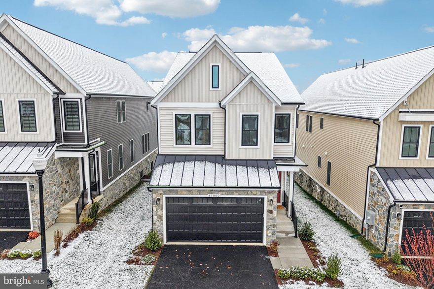 This nearly new Van Metre Caledon model in the sold out Brambleton’s West Park neighborhood offers over 3,500 finished square feet across three levels, with 5 bedrooms and 4.5 bathrooms and a thoughtfully designed layout that blends open living with flexible spaces.

The main level features 9-foot ceilings and luxury vinyl plank flooring throughout. A bright, open floor plan connects the great room, dining area, and kitchen, creating a comfortable space for everyday living and entertaining. Just off the main living area is a flex room that works well as a home office, playroom, or sitting area depending on your needs.

The kitchen sits at the center of the home and features quartz countertops, upgraded cabinetry, a tile backsplash, stainless steel appliances, and a large island with seating. It offers plenty of counter space and storage while staying connected to the main living areas.

Upstairs, the primary suite provides a spacious retreat with a coffered ceiling, two walk-in closets, and a well-appointed bathroom with double vanities and an oversized frameless glass shower with a built-in bench. Three additional bedrooms and two full bathrooms are located on the same level, along with a convenient upstairs laundry room.

The finished lower level adds valuable living space with a large rec room that works well as a media room, playroom, or home gym. An additional bedroom and full bathroom on this level provide a comfortable setup for guests or extended family.

Additional features include a front-load two-car garage with EV charging capability, a practical family entry area, and a sizable backyard with room to relax, garden, or entertain outdoors.

Located in the Brambleton community, residents enjoy access to miles of walking trails, parks, pools, playgrounds, and a wide range of neighborhood amenities. Brambleton Town Center, just minutes away, offers convenient shopping, dining, a movie theater, and community events throughout the year.

With modern construction, a well-designed floor plan, and access to one of Loudoun County’s most sought-after communities, this home offers the benefits of newer construction without the wait.