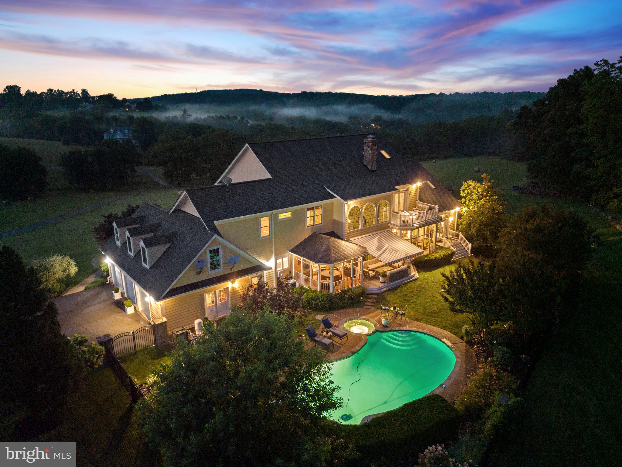 Nestled within the rolling hills of Paeonian Springs, 40959 Pacer Ln presents an unparalleled opportunity to own a slice of Loudoun County's idyllic countryside. This exceptional estate, sprawling across more than 14 acres of open land, offers a sanctuary of privacy and breathtaking natural beauty. Imagine waking to panoramic sunrises and unwinding with spectacular sunsets, all visible from the expansive front porch, a true testament to the property's prime location. This is a residence for those who seek a deep connection with the outdoors, a place where the changing seasons paint a vibrant tapestry of color and the wooded backyard provides a tranquil, private retreat. While enjoying a tranquil rural setting, you're conveniently located just minutes from vibrant downtown Leesburg, VA, and a mere 22 miles to Dulles International Airport.
The outdoor living spaces are designed for both grand entertaining and serene relaxation. A 20-foot diameter stone firepit, surrounded by a flagstone hardscape, creates an inviting ambiance for gatherings under the stars. A sparkling pool with built-in hot tub offers resort-style amenities, while covered porches off the kitchen and first-floor primary suite provide seamless indoor-outdoor living (2nd hot tub is freestanding). A Trexx deck offers ample space for al fresco dining and enjoying the picturesque surroundings. The entire 14-acre property is secured with an invisible fence, and an automatic irrigation system ensures lush, green lawns across three acres. An oversized three-car garage provides ample space for vehicles and storage.
Inside, the home exudes elegance and sophistication. The great room, features a floor-to-ceiling masonry fireplace, new porcelain tile flooring with electric under-floor heating, and tinted windows for energy efficiency. The remodeled kitchen, boasts custom cabinetry, countertops, modern flooring, dual dishwashers, and updated appliances and lighting. Two luxurious primary bedroom suites provide ultimate comfort and privacy. The first-floor master bedroom suite is perfect for the person who is looking for one level living, while the upper-level suite includes new red oak hardwood floors, light fixtures, large walk-in closet, a sitting room, fireplace, and private deck with elegant French doors. A refined library with custom wood bookshelves and a fireplace offers a tranquil space for reading and reflection. The upper level also includes two additional bedrooms, each with its own en-suite bathroom, and a convenient laundry room.
The walk-out lower level is an entertainer's dream, featuring a masculine bar area with custom wood cabinets, a club chair seating area with a fireplace, a pool table, a shuffleboard game room, and a fifth bedroom with an en-suite bath. This space, transformed from a mother-in-law suite in 2015 with a $150,000 renovation, includes custom built-ins, hardwood floors, and updated lighting.
The home has been meticulously updated with modern amenities, including a new well installed in 2020, updated pool equipment, HVAC units, a gas water heater, and washer and dryer. A whole-house Sonos sound system with 15 sets of speakers provides seamless audio throughout the home and outdoor spaces. A durable Grand Manor architectural shingle roof with a 50-year warranty protects the residence. This exceptional property at 40959 Pacer Ln offers a rare opportunity to experience the best of Loudoun County living, where luxury, privacy, and natural surroundings come together beautifully.
Updates: Roof (2025) Kitchen (2023), Basement Bar/Pub Area (2015), Master Bedroom Suite (2020), Great Room (2023), 20' diameter stone fire-pit (built in 2015), Updated Trex back deck (2022), Invisible fence surrounds the entire 14-acre property, pool equipment (motor, heater, pump, and filter replaced in 2020), Main Level HVAC (2022), Upstairs HVAC (2020), Gas Water Heater (2020). More info available upon request.