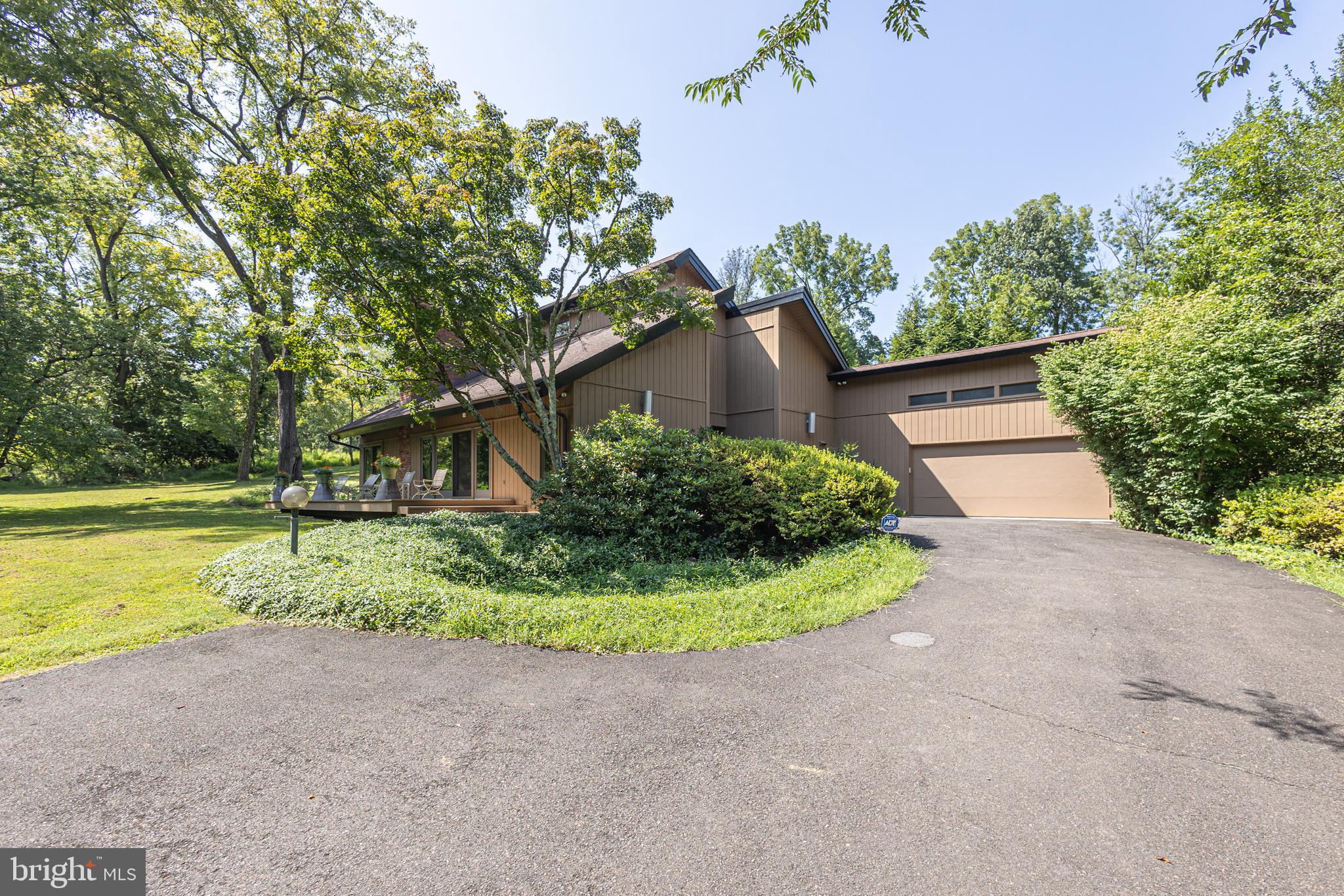 A rare opportunity awaits with this custom-built, Mid-century inspired residence, that is thoughtfully designed with a first-floor primary suite. Welcome to Sunny Knolls, where you will experience the best of both worlds; a private sanctuary within a walkable neighborhood. Gleaming hardwood floors—extending through much of the home—and a soft, neutral palette establish a sense of openness and harmony across the living, dining, and kitchen areas. A welcoming vestibule leads into the sunlit, vaulted great room, where a striking floor-to-ceiling, two-sided brick wood-burning fireplace commands attention. Walls of windows frame panoramic views of the front lawn while offering seamless access to an expansive deck. On the opposite side of the fireplace, a versatile sitting room provides the perfect setting for quiet relaxation or lively conversation both indoors or out on the adjoining deck. The main-level primary suite is a peaceful retreat, with a spacious, light-filled bedroom and an ensuite bath that connects to a large laundry room for everyday ease. Designed for both intimate gatherings and grand entertaining, the kitchen and dining area easily accommodate a crowd and open through sliding glass doors to a generous patio—blending indoor and outdoor living. The gourmet eat-in kitchen features GE Profile stainless steel appliances, quartz countertops, and abundant cabinetry, enhanced by a new Bosch dishwasher, delivering both timeless elegance and modern functionality. Upstairs, one additional bedroom and a flexible bonus room share a beautifully appointed hall bath. Beyond the interior, an exceptionally deep and private yard creates a serene backdrop for outdoor enjoyment. Set within the highly regarded Pennsbury School District and moments from parks, golf courses, and the vibrant boroughs of Newtown and Yardley, this exceptional property offers a rare fusion of comfort, style, and convenience—ready to begin its next chapter.