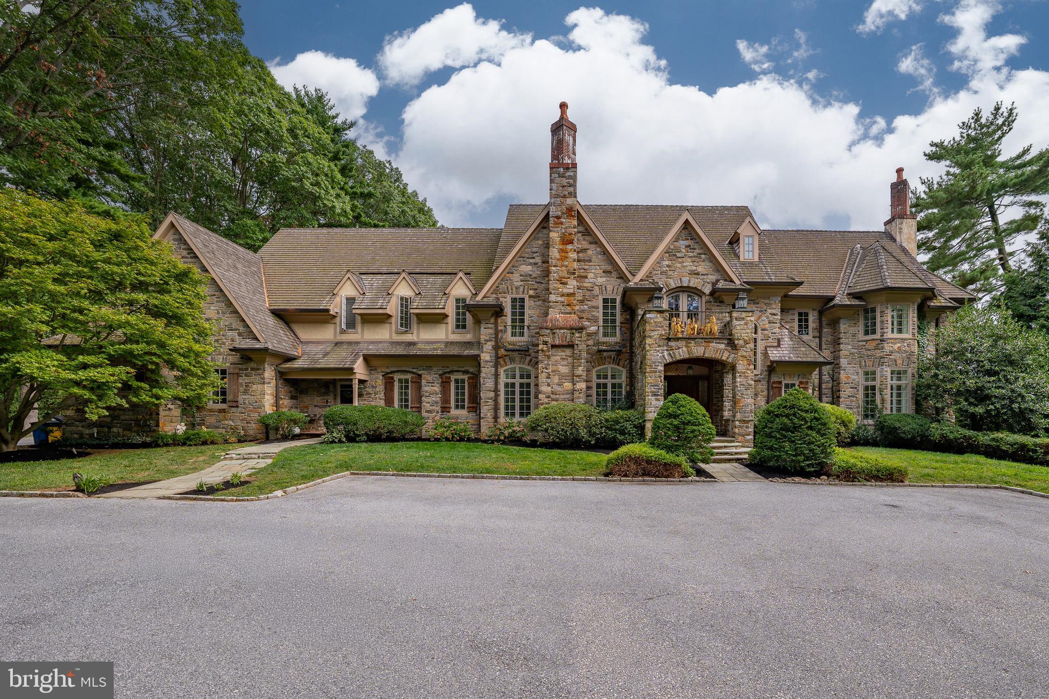 Set behind private gates on 1.16 acres, this magnificent 10,488 sq ft Bryn Mawr Estate blends old-world craftsmanship with modern luxury. Masterfully built by Michael Cutler Builders and designed by Scott McIntyre, the Stone Manor showcases soaring 10+ ft ceilings, walnut hardwood floors, an elevator, and grand proportions throughout its 5 Bedrooms, 7 Full Baths, and 2 Powder Rooms. A gracious courtyard leads to a marble foyer and formal living room with coffered ceilings and a gas fireplace. Additional highlights include a sun-filled conservatory, richly paneled library with Halkett millwork and French doors to the patio, and an elegant dining room with a gas fireplace and butler’s pantry. At the heart of the home, the Clive Christian gourmet kitchen features a walk-in pantry, Sub-Zero refrigerators and freezer, Wolf range, double ovens, and a breakfast area opening to the family room dark wood coiffured ceiling and stone fireplace creating a warm and cozy ambiance. A mudroom with cubbies and two powder rooms complete this level. The primary suite retreat offers dual walk-in closets, two spa-like baths with marble finishes, a sitting room with a fireplace, and a private balcony overlooking the grounds. Four additional en suite bedrooms and a cedar closet complete the second level. The walkout lower level is designed for entertainment and wellness with a theater, gym, sauna, spa, wine cellar, second kitchen, and family room. Exceptional details include a Lutron lighting system, custom shutters, a whole-house generator, an irrigation system, a 3-car garage, and a walk-up attic. Outdoor living is enhanced by a rear patio with a stone fireplace—ideal for year-round gatherings. Located on one of the Main Line’s most prestigious streets in the award-winning Lower Merion School District, this estate offers unmatched elegance, privacy, and convenience—just minutes to the R5 train, dining, and Center City.