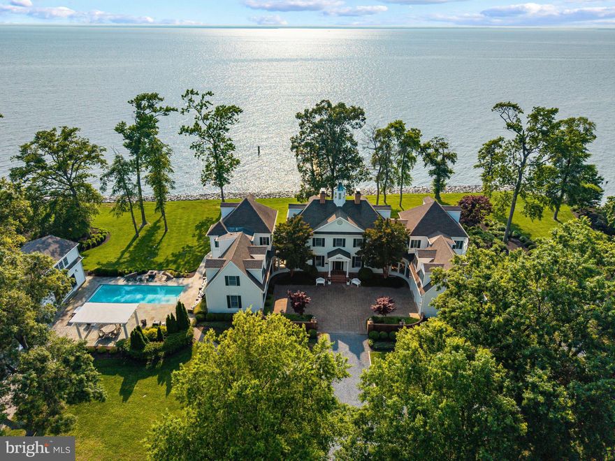 Elegant waterfront home resting on the banks of the Chesapeake Bay nestled in a bucolic setting with stunning sunset views just minutes from the Bay Bridge. Experience a rare blend of elegance, privacy, and panoramic Chesapeake Bay views from this extraordinary 19-acre waterfront estate. This stunning residence is designed for both refined living and effortless entertaining, with a thoughtfully curated layout and resort-style amenities throughout. The heart of the home is a striking architectural masterpiece featuring gracefully curved walls of windows at both ends of this sprawling home, framing breathtaking water vistas and filling the interior with natural light. The gourmet kitchen serves as the central hub, perfectly positioned between expansive living spaces ideal for gathering or relaxing. A main-level ensuite bedroom offers convenience and comfort, and a second ensuite bedroom directly above links to the extraordinary catwalk that overlooks the soaring living room below and provides access to the balconies overlooking the yard and the Bay.  Head upstairs of the main home to experience the luxurious primary suite. A true sanctuary this suite is complete with a grand sitting room/office area with fireplace, soaring ceilings, a private balcony, and a spacious screened-in deck where you can soak in the sweeping views of the Bay. A guest bedroom with an elegant bath and a well-placed laundry room complete this floor. The uppermost level features a generous walk-in closet, full bath, and two versatile bedroom areas. Step outside into your personal paradise! The resort-style pool area is accented by exquisite hardscaping, offering multiple areas for lounging, entertaining, and dining al fresco. A sunken fire pit sets the stage for magical evenings under the stars. The separate pool house is a fully equipped guest retreat with a kitchen, living area, bedroom, and full bath. The private pier is equipped with a boat lift, multiple slips and is a quick 15-mile cruise by boat to St. Michael's or the Annapolis harbor. Additional special features include a private studio space/detached garage currently used as a gym, a fairy-tale tree-lined driveway leading to a two-car attached garage, and a stately car court. With its unparalleled setting, inspired design, and luxurious amenities, this Chesapeake Bay estate is truly one-of-a-kind — a place where every day feels like a getaway. Welcome Home!