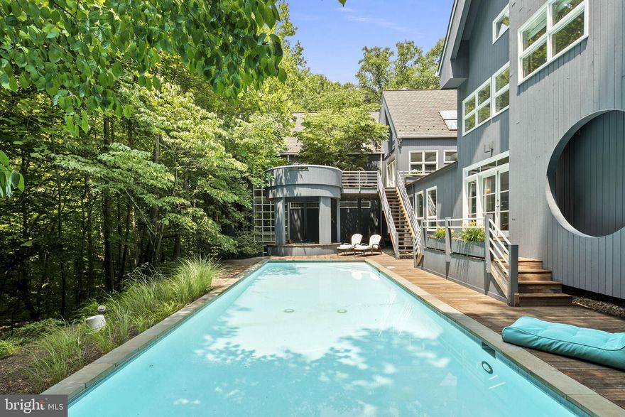 Resort-style living without leaving home!! Now is your chance to take advantage of this significant price reduction and an amazing deal for the savvy buyer! The gorgeous 44' pool has been completely resurfaced and painted and a new electric cover was installed! Architect PD Gravitts built this Stunning Modern home for himself and his family.  Three miles from the Potomac River, this exciting home includes an outdoor oasis with decks, a creek meandering through the property, and walking or hiking trails on five private acres.  Bowa Builders renovated the house, adding a bedroom suite including a bathroom, a fabulous laundry room, a full bath in the guest wing, and a heated three-car garage with unfinished space above including dormer windows, skylights, and endless possibilities.  The long, newly paved driveway flanked by custom stone walls welcomes you and a stunning breezeway connects to the house.
As you enter, notice the soaring two-story living and dining areas washed with light from skylights and walls of windows. Beautiful treed views are enjoyed throughout the house, giving a tree-house effect while allowing the light to flood in. The sleek kitchen has an island with a gas cooktop, white modern cabinetry, two Wolf ovens, a Subzero Fridge, a large walk-in pantry-catering area with an extra fridge, and a casual dining area. Glass doors give access to the deck and outdoor living space. There are a total of five bedrooms and five and a half baths. Three bedrooms are ensuite in the main part of the house. One is currently used as a gym with newer wood floors, featuring doors leading to a lower deck overlooking lush vistas and the creek. The fourth and fifth bedrooms are in the guest wing of the house, accessed by a spa-like walkway lined with windows viewing the pool. Visual and architectural interest is found in every room. Don’t miss this unique opportunity to own this blissfully peaceful, spectacular contemporary in a wonderful Great Falls neighborhood near Auberge Chez Francois Restaurant and Riverbend Country Club, with quick access to 495, and Dulles Airport. Make sure to watch the property video!