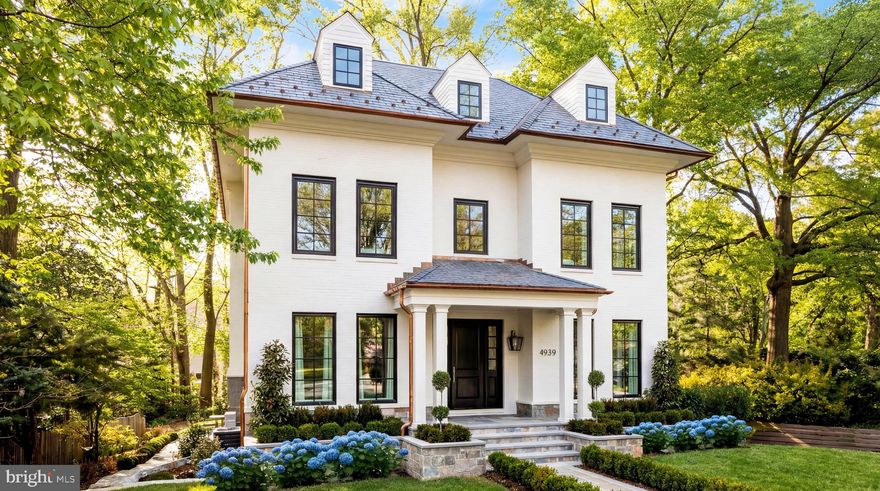 A grand architectural statement in the heart of Spring Valley, 4939 Quebec Street NW is a newly constructed masterpiece by Akseizer Residential, envisioned by Akseizer Design Group as a study in timeless craftsmanship and modern elegance. Executed from the ground up, the residence embodies a rare union of classical detail, transitional design, and advanced systems.

Perfectly sited on a deep lot along one of the neighborhood’s most distinguished streets, the exterior presents a quietly commanding presence defined by custom-profiled solid mahogany doors, Quaker windows, and disciplined architectural symmetry. A central flagstone path provides a gracious introduction.

Inside, wide-plank rift- and quartersawn white oak floors extend throughout, paired with a custom molding package including substantial baseboards, layered crown, and refined door casings. Custom paneled stairway walls and seven-foot solid-core doors finished in lacquer and paired with polished nickel Baldwin hardware create a cohesive aesthetic.

Formal living and dining rooms flank the reception foyer in a traditional center hall configuration, complemented by a richly appointed study featuring black lacquered pocket doors and a gas fireplace set in Pietra Grey marble.

The main living areas are anchored by a kitchen and family room where form and function coexist seamlessly. Custom cabinetry with solid white oak drawers is complemented by White Calacatta stone surfaces, including an integrated sink and waterfall island. Appliances by Wolf, Sub-Zero, and Cove are joined by Urban Electric pendants, Waterworks fixtures, and solid brass hardware. A fully equipped scullery connects to the formal dining room.

The adjoining family room centers around a gas fireplace framed in Calacatta marble with a white oak mantel and integrated television. French doors open to a screened-in porch, extending the living area outdoors.

Privately situated at the rear of the upper level, the primary suite features vaulted ceilings and bespoke millwork. The dressing room offers custom white oak cabinetry, fluted detailing, illuminated storage, a concealed laundry station, and a vanity with Calacatta stone top.

Clad in Calacatta Gold marble, the primary bath offers heated floors, dual vanities, a freestanding Waterworks soaking tub, and polished nickel fixtures.

Three secondary bedrooms share two appointed baths featuring marble tile and Waterworks fixtures. An expansive top-level loft introduces an additional bedroom and full bath.

The fully above-grade lower level features a lounge with wet bar and a flexible second living space. A separate area is ideal as a gym or private bedroom with en-suite bath. The level walks out to a private rear lawn via a covered loggia with an outdoor fireplace. A feasible rear yard expansion and pool installation is shown in our virtual tour, adding additional space and amenity flexibility. 

Engineered for comfort and discretion, the home includes sound attenuation, spray foam insulation, Lutron RA3 lighting control, distributed Sonos audio, full-home networking, security cameras, wireless HVAC control, and a private elevator. The garage includes custom wood doors and EV pre-wiring.

Executed with extraordinary attention to detail and reverence for enduring design, 4939 Quebec Street NW is a definitive Spring Valley residence exemplifying comfort and timeless elegance.