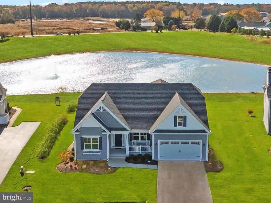 Located in the award-winning 55+ community of Independence by Schell Brothers, this meticulously maintained 3BR, 2BA plus flex room, single-level home blends designer style with water-view tranquility. Positioned directly pond-front, every rear window frames peaceful views of the sparkling fountain and open sky. Inside, the open-concept floor plan highlights the 2ft expanded living area,  floor-to-ceiling windows, rich wood flooring, and upgraded moldings. The living area centers around an electric fireplace with custom stone surround and built-in shelving, creating a perfect focal point for gatherings. The gourmet kitchen features custom soft-close cabinetry, quartz countertops, modern stainless steel appliances (oven never used), and an oversized island ideal for entertaining. The primary suite offers serene water views and a spa-style bath with a frameless glass walk-in shower. A custom pocket door leads directly to the laundry room for everyday convenience.  The flex room can be used as a 4th bedroom, office, or craft room. Additional highlights include custom window treatments, a whole-house generator, a Honeywell UV air purifier system, and a security system with exterior cameras. Light-filled rooms and thoughtful details make this residence truly model-home quality. Enjoy the benefits of the seller’s Pay Ahead program, resulting in lower recreation fees for the buyer. Independence’s 24,000-square-foot clubhouse offers resort-style amenities: indoor/outdoor pools, fitness and yoga studios, sauna, ballroom, billiards, pickleball, tennis, bar/lounge, dog park, and miles of walking paths. Conveniently located near Harris Teeter (1.0 mi), Beebe Medical at Millsboro (2.3 mi), and Lewes and Rehoboth Beaches (10–13 mi), this home provides an ideal blend of peaceful living and coastal convenience. Immaculate, thoughtfully upgraded, and move-in ready—this is pond-front living at its best.