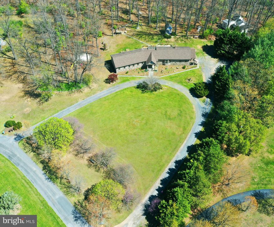 WELCOME HOME TO A SPECIAL PLACE WHERE MEMORIES ARE MADE! RELAXING RETREAT ON 5 ACRES WITH A SPECTACULAR, ONE-OF-A-KIND CUSTOM HOME.  A contemporary rancher with more than 2,500 square feet, 3 bedrooms and 2 1/2 baths. Near Winchester and commuter convenient to Rt. 7 and I-81 - but so restful and inviting that you'll never want to leave!  You can even bring the critters - horses, cows, sheep and chickens are allowed! All on one level. Unique, one-owner home that a builder lovingly crafted for his family. Spectacular stone front. Beautiful grounds with a landscaped front lawn and woods in the back. Sweeping circular driveway and a tarmac that could accommodate a 25x40 garage.  The back yard offers a firepit area with benches; a colorful playhouse with a loft, electricity and insulation; and a playset with swings, sandbox and a slide.  A meandering path through the woods leads to a camping spot with a seasonal stream. Spacious rooms throughout with hardwood, tile and luxury plan vinyl floors.  Elegant entry foyer with tile floor, crown molding, chair rail and shadow box. Hallway with curved wall and framed areas for hanging photos. Great room with a 12-foot cathedral ceiling, dramatic stone fireplace with a hearth and mantle, and built-in cabinets with counter space for books and displaying artwork. A bay window with a space for plants. Beautiful family room with wood paneling, 10-foot ceiling, stone wall, Scandinavian wood stove, TV nook and built-in counters for computers could double as an office/library. There's a window seat and hooks for coats and jackets in the nearby hall. The roomy kitchen is bright and cheerful with skylights, pendant lights and a 5-foot garden window over the double sink. Cozy dining area. Stainless steel appliances. Shaker-style natural hickory cabinets, including some with glass fronts for displaying dishes and glassware. Sliding doors off the great room and kitchen lead to a 16x48 deck that overlooks the woods.  The primary bedroom suite has two walk-in closets, a built-in queen-size bed and an elegant primary bath with tiled walls, oval window, double-sink vanity and walk-in shower with two shower heads.  Separate laundry room with shelves. Attached storage room plus two large sheds with electricity.  Raised garden beds. The house is served by a 2-zone heat pump and a 3-bedroom, gravity-flow conventional septic. The community offers access to  Opequon Creek for swimming and kayaking.