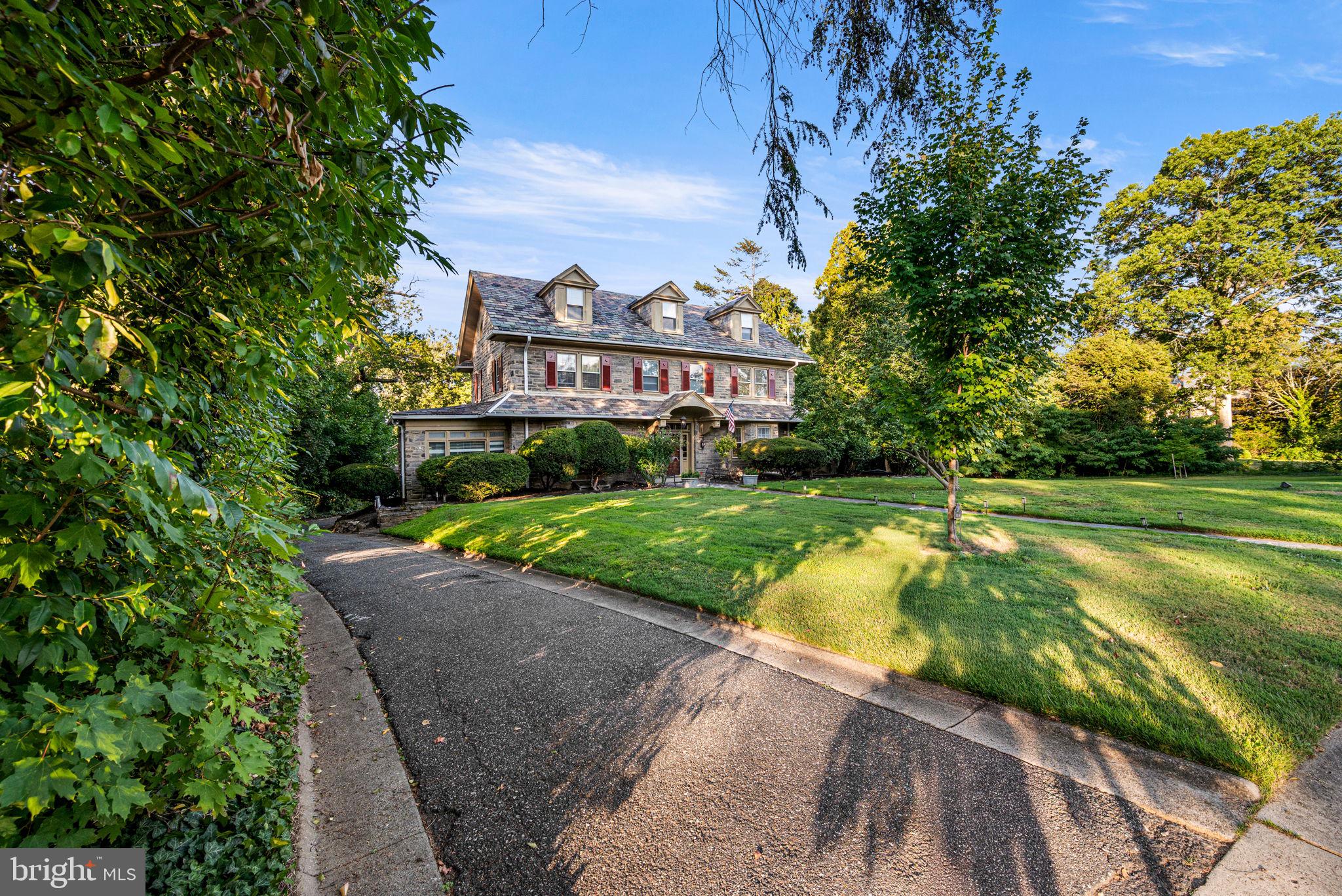 Welcome to 27 Latham Park, a rare opportunity to own a piece of history in one of Montgomery County’s most iconic neighborhoods. Nestled inside the La Mott Historic District, Latham Park is widely recognized as the first gated community in Pennsylvania, offering privacy, exclusivity, and timeless elegance. Perched on an expansive 1+ acre lot, this stone Colonial built in 1929 blends historic charm with thoughtful modern updates. From the moment you enter, the home greets you with its grand staircase, original hardwood floors, crown molding, built-ins, and not one but two fireplaces - a wood-burning fireplace in the formal living room and a stone gas fireplace in the family room. The kitchen has been beautifully upgraded with granite countertops, soft close cabinetry and drawers, and stainless steel appliances, complemented by a large walk-in pantry and formal dining room. The main level also includes a bright sunroom, convenient half bath, and access to to the expansive slate patio. Follow the grand staircase upstairs and find, the home offers three spacious bedrooms and two full bathrooms, including a Primary Suite with an upgraded ensuite bath and a walk-in dressing room. The third level expands the possibilities for guest rooms or office space with three bedrooms and two full bathrooms, and has two large cedar closets providing abundant storage. The lower level features a partially finished walk-out basement with its own half bath - recently waterproofed for peace of mind - offering flexible space for recreation, fitness, or a home office. Important system upgrades include newer heating and central air conditioning, as well as updated electrical circuit breaker panels and a newer flat roof over the kitchen. Outside, the property shines with a detached two-car garage, equipped with a new roof, new automatic doors, and an oversized upper level for storage, ample driveway parking, and a peaceful rear patio overlooking a private, park-like backyard. The nominal HOA fee covers snow removal, landscaping, and common area maintenance - preserving the integrity and beauty of this historic enclave. Located just minutes from parks, public transportation, and community landmarks like the Frank Lloyd Wright-designed Beth Sholom Synagogue, the shops and cafés on High School Road, and the historic Elkins Estate, this home is more than a residence - it’s an invitation to live in one of Elkins Park’s most celebrated communities.