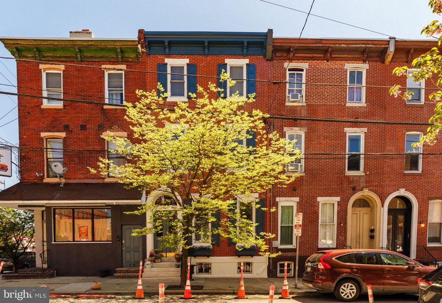 This home sits in that sweet spot that Philadelphia does so well: historic, but not frozen; elegant, but not precious; architecturally grounded, yet deeply personal. Welcome to 871 N 26th Street, lovingly known by neighbors as “the dog treat house”, a quietly confident Fairmount rowhome that doesn’t need to shout to be noticed. It simply is.

Rooted in the late 19th century, the home carries Federal and Italianate influences in its bones, but what makes it truly special is how gracefully it has been cared for and layered over time. Nothing feels forced. Nothing feels overly polished. Instead, there’s a sense of ease, of a home that has evolved thoughtfully, with intention and respect for its past.

The story begins at the street. There’s a rhythm to the block: warm red brick, tall windows, a sense of continuity, but this home gently sets itself apart. An arched stone surround frames the entry, while a bracketed cornice adds texture overhead. The double doors painted a deep, moody blue and accented with brass hardware, sit beneath a graceful transom. Flowering window boxes, a weathered marble front stoop, a tree casting dappled light across the brick: it’s not just architecture, it’s atmosphere.

Step inside, and the home offers a quiet pause. A vestibule wrapped in rich William Morris wallpaper feels intimate, unexpected, and entirely charming. It’s a reminder that homes of this era were designed with transitions and a sense of arrival. This one still honors that beautifully.

Beyond, the main living spaces unfold with quiet confidence. An arched opening frames the living and dining rooms, elevating the everyday in a way that feels almost cinematic. Sunlight moves gently across wide-plank yellow pine floors, worn to a soft glow by more than a century of life. It’s easy to imagine long dinners here, conversations that linger, music playing somewhere in the background.

The kitchen is where past and present meet most seamlessly. A generous quartz island anchors the space, ready for morning coffee or late-night gatherings, while a showstopping blue La Cornue range --one of four ovens -- makes a statement that’s both bold and timeless. GE Café appliances and a wine fridge bring modern ease, while an original butler’s cupboard, sourced from a monastery, adds a layer of history you simply can’t replicate. Just beyond, a sun-filled breakfast nook with built-in banquette seating and a pass-through window creates an effortless connection to the outdoors.

Out back, a Trex deck framed in lattice extends the living space, perfect for summer dinners, container gardens, or a quiet glass of wine at dusk. A charming hand-stenciled powder room completes the main level with a touch of personality.

Upstairs, the second floor feels like a retreat. The primary bedroom welcomes you with soft light filtering through plantation shutters in a graceful bay window. A decorative marble fireplace anchors the room, while a custom wardrobe adds function . The en-suite marble bath leans quietly luxurious, with radiant heated floors and a steam shower that rivals a boutique hotel. A second bedroom and a thoughtfully designed laundry room complete the floor.

The third floor continues the story with three additional bedrooms, each filled with warmth, character, and beautiful natural light, along with a full bath, offering privacy for guests.

And then there’s the neighborhood. Morning espresso at Musette, an afternoon stroll along the Schuylkill River Trail, weekends spent wandering the Parkway, modeled after Paris’s Champs-Élysées, and visits to the Art Museum, The Barnes, and Calder Gardens. It’s all just moments away, yet the street itself remains quiet, tree-lined, and wonderfully livable.

This is more than a beautiful house. It is a home with atmosphere, romance, and soul, where history and modern life coexist with ease. Timeless, thoughtful, and deeply inviting. An extraordinary offering.