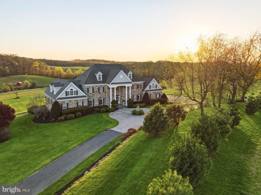 Set across approximately 115 extraordinary acres in the rolling countryside of White Hall, this landmark estate presents a rare opportunity to own a custom hand-built masterpiece by renowned builder Art Wood, whose name is synonymous with exceptional craftsmanship, architectural integrity, and enduring quality throughout Harford and Baltimore Counties. Privately sited amid panoramic rural vistas, the property offers an unmatched sense of scale, beauty, and permanence, with manicured grounds, extensive stone hardscaping, elegant retaining walls, covered patios, curated walkways, and a striking entry courtyard that creates an unforgettable arrival. Constructed in 2006, the main residence encompasses more than 10,000 square feet of finished living space across four finished levels, each thoughtfully designed to balance grandeur, comfort, and function. With 9 bedrooms, 5 full baths, and 3 half baths, the home is exceptionally appointed with an elevator, geothermal heating, a propane-powered whole-house generator, and a 3-car garage. Luxury spaces throughout include a private in-law apartment, theater room, game room, wet bar, library, fitness room, art room, and substantial storage, creating a residence equally suited for elegant entertaining, multigenerational living, and private retreat. A grand courtyard entry opens to a dramatic two-story foyer showcasing gleaming porcelain flooring, a sweeping dual curved Brazilian cherry staircase, retractable crystal chandelier, and an impressive overlook above. The soaring family room is anchored by a two-sided fireplace and framed by oversized windows that capture the surrounding countryside. At the heart of the home, the gourmet kitchen is richly appointed with granite countertops, Brazilian cherry flooring, a substantial center island, Viking gas range, Italian carved marble stove canopy, Italian tilework, wine storage, a walk-in pantry, and a sunlit dining area with French doors leading to the expansive elevated deck. The main-level primary suite offers a luxurious private retreat with soaring two-story ceilings, a fireplace, private deck access, two oversized walk-in closets with dressing areas and window seats, and a spa-inspired bath featuring a soaking tub, tile shower, dual vanities, separate water closets, and custom cherry cabinetry. Formal living and dining rooms, a mudroom, spacious laundry room, and additional refined gathering spaces further enhance the main level. Upper levels continue the home’s remarkable scale with multiple bedrooms, full baths, bonus spaces, exercise area, and storage, while the walkout lower level is designed for entertaining with a raised-hearth stone fireplace, theater with recliner seating, game area, wet bar, and private in-law quarters complete with a full kitchen and bath. Beyond the main residence, the estate includes a separate 3-bedroom, 2.5-bath Cape Cod tenant house built in 2007, offering exceptional flexibility for guests, extended family, or on-site management. Equestrian and agricultural amenities further distinguish the property and include a bank barn, 9-stall horse barn, 90x42 machinery shed, fenced pastures, stream, pond with island, wooded acreage, and productive tillable land. This is far more than a home. It is a legacy estate of rare caliber, hand-built by Art Wood and offering an extraordinary combination of craftsmanship, acreage, privacy, and presence in one of Harford County’s most scenic countryside settings.