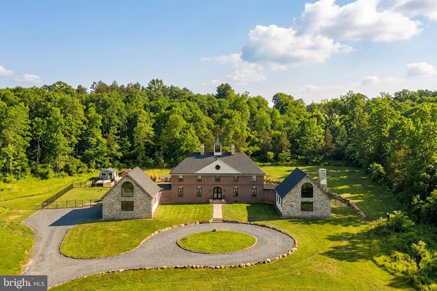Offered in its entirety across two parcels totaling 35 acres, this newly and exquisitely renovated estate is a masterclass in elevated design, where timeless architecture meets modern luxury. Every space has been thoughtfully reimagined with an uncompromising attention to detail, craftsmanship, and visual harmony.
A dramatic foyer welcomes you with honed black-and-white marble floors, a gorgeous sweeping double staircase, and striking antique lighting immediately setting the tone for the refined interiors beyond. Wide-plank oak hardwood floors flow throughout the main level, complemented by curated finishes and abundant natural light that enhance the home’s sophisticated yet inviting atmosphere. At the heart of the home is a show-stopping designer kitchen, crafted as both a statement and a gathering space. Custom cabinetry is paired with dramatic Taj Mahal and Black Diamond quartzite, fluted marble detailing, and bespoke walnut millwork that brings warmth and architectural depth. An expansive island serves as the centerpiece of the space, complemented by a fully integrated, premium appliance suite that balances refined aesthetics with effortless functionality. Built-in wine storage adds visual impact and practicality, while a dedicated coffee bar creates a refined, café-inspired experience at home. Just beyond, a beautifully appointed butler’s pantry offers additional prep and storage space, framed by elegant arched French walnut doors that create a striking architectural transition between spaces. The kitchen flows effortlessly into the surrounding living areas, maintaining a sense of openness while allowing each space its own distinct character. The living room is warm, inviting, and architecturally rich, anchored by a stunning fluted fireplace framed in stone and custom walnut millwork. Built-in shelving provides tailored display and media storage, while soft textures, thoughtful proportions, and generous natural light make the space ideal for both relaxed evenings and sophisticated gatherings. The connected barn room is a truly spectacular space, defined by its soaring cathedral ceiling and dramatic exposed beams that create a sense of volume and architectural presence rarely found in modern renovations. Warm wood floors enhance the room’s character while maintaining a refined aesthetic. A character-rich, antique-inspired dry bar anchors the space, while the lofted overlook and open layout further elevate its sense of grandeur. Expansive windows capture breathtaking sunset views, making this an ideal setting for entertaining, game nights, or unforgettable gatherings year-round.
Upstairs, the private quarters continue the home’s elevated aesthetic. The primary suite is a serene sanctuary offering generous proportions, private balcony access, custom closets, and a spa-inspired bath complete with a generously sized custom shower, an elegant soaking tub, and heated floors. Three additional bedrooms are spacious and thoughtfully designed, each showcasing unique details such as custom millwork and flexible layouts ideal for guests, work, or creative use. The three-car garage wing offers exceptional flexibility with additional living potential—ideal for a home office, guest suite, or studio—while enjoying spectacular, far-reaching views and breathtaking sunsets that elevate the space into something truly special.
Outdoors, the property offers a private, resort-like setting with expansive lawn, mature trees, and thoughtfully designed landscaping. Custom stone boulders and natural stone walls add texture and architectural interest, while a resort-style pool and pavilion create a striking focal point for outdoor living. Sweeping views and unforgettable sunsets complete this serene and private retreat. 1400 Fairhill Road is a rare opportunity to own a fully reimagined luxury residence where exceptional design, craftsmanship, and livability come together in perfect balance.