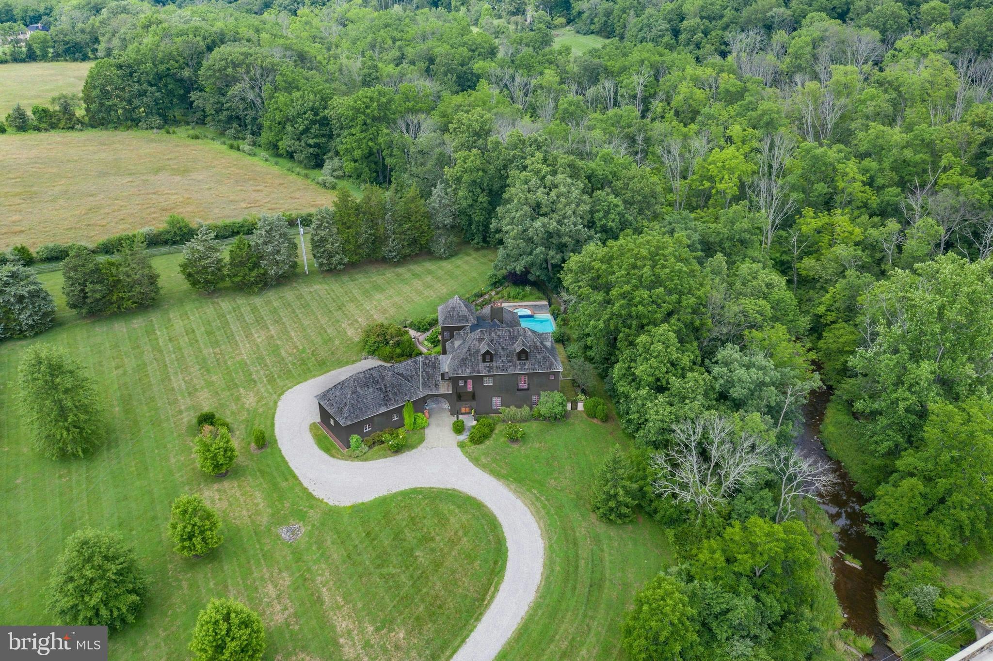 Renovated in 2021 and set on 3 private acres with views over pristine Cooks Creek, this stunning villa is a rare blend of 19th century touches & outstanding modern luxuries. European architecture is married to the classic PA environs through clever design & construction. A cedar shake roof, textured stucco exterior & antique c.1910 French doors provide focal points. At every turn there is meticulous attention given to the patina of the plastered walls, antique wood flooring & placement of elegant windows, arches, & doorways.
The breathtaking great room has radiant-heated limestone floors, a grand ceiling height w/century old beams, a fireplace with 1820’s lintel, antique doors from New Orleans, multiple arched doorways & opens to a patio perched above Cooks creek. The kitchen is a cook’s dream, equipped w/ an AGA range, gourmet appliances, limestone counters, farmhouse sink, separate prep kitchen & fireplace. The luxurious primary suite has a fireplace, 3 balconies, a jetted tub positioned in a windowed alcove, & bath with heated floor & steam shower. 2 en-suite BRs w/balconies & a separate 2021 office complete the 2nd floor, while a BR, family room & full bath are on the 3rd floor. The heated 3-car garage is connected by a porte cochere.
The gorgeous pool, spa & terrace are spectacular vantage points for entertaining, with Cooks Creek providing an incomparable backdrop. Adjacent preserved lands ensure that this breathtaking beauty will always remain.
