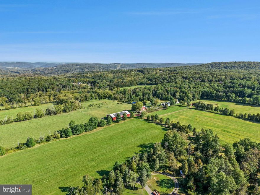 Bucks County farmhouses are defined by their settings and their position on their acreage, overlooking their fields and pastures, with long driveways leading past bank barns and farm buildings. Wheaton Fields Farm is one of the finest examples of these storied properties, boasting 50 acres of woods, fields, pond and even an orchard.
At Wheaton Fields, approach to the cluster of picturesque farm buildings is down a quarter mile drive, nicely removed from a quiet country road. The quintessential 1800’s pointed stone colonial, with rocking chair front porch, has been renovated and enhanced. A 2024 great room addition has three walls of glass, an exposed stone wall, wet bar, skylights, and fireplace, all opening to the sandstone patio with long distance views over the acreage and beyond. Pine, hickory and tile floors span both levels of the home. Throughout, 3 fireplaces, mullioned glass windows with deep windowsills, and period hardware attest to the classic Bucks County farmhouse character. Completing the first floor is a cozy living room with fireplace, dining room and charming country kitchen. On the second floor, there is an open and airy primary suite, bath and two additional bedrooms. 
Outside, there are multiple buildings that have been cleverly converted into areas for guests, family, or hobbies. A picture-perfect 2017 pool house was designed to complete the original farmhouse with its own stone exterior. The stunning kitchen and great room with radiant heated floor opening to a covered patio and heated saltwater pool overlooking the orchard and greenhouse. Upstairs, a full bath and two additional studio rooms make this an ideal space for visitors. Nearby, one of the original farm buildings now boasts 3 charming cottages, 2.5 baths, as well as a family room, kitchen and laundry facilities. The three story bank barn includes a wing that has been converted into a studio, with bath and kitchenette. The 2015 pole barn will store every toy and farm essential and has solar panels sufficient to run the whole property. The private pond and dock beckon an afternoon on the water. Finally, there is a greenhouse and a fenced orchard with mature apple, pear, peach and plum trees.
This solar-powered property with generator lets you relax and invite a crowd for summer weekends, winter escapes, and every holiday. Whether a full-time residence or a weekend retreat, special occasions and other outside events will be celebrated here with joy. The views from the porch and patios provide an ever-changing panorama of seasonal colors and simple evening relaxation under the stars.
Wheaton Fields is the perfect farm property, enhanced by elements from a bygone era and nestled in a secluded Bucks County setting. This clever design allows for use as a family compound or for multi-generational living. This private paradise loses touch with the world just over the hills, yet is still within easy driving distance to magic weekends of Bucks County dining, antiquing and recreation.
