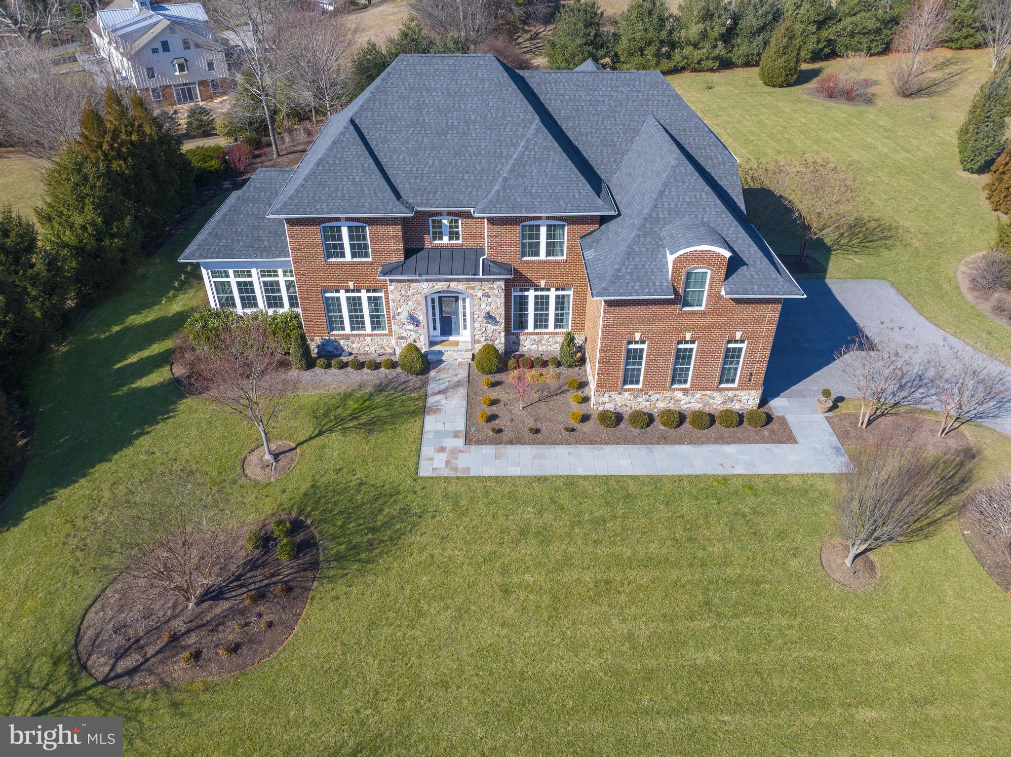 Built to perfection in 2014, this beautiful home in Scaleby Farm boasts more than $340,000 in upgrades and custom features from the base home model. Situated on a 2.2 acre lot and featuring approximately 7,700 sf of finished living space, this stunning property offers everything that appeals to discerning buyers. The curb appeal is evident by the use of brick and stone for the exterior and the landscaping designed by Robinson Anderson Summers Inc, a firm that has done landscaping for US Botanical Gardens and Nemours Mansions and Gardens. Quality and craftsmanship prevail in the architectural features, fine materials and design elements used throughout the home. Upon entering, one immediately appreciates the thoughtfully designed and appointed living spaces, creating a timeless and inviting home. The foyer features gleaming hardwood floors, a grand two-story staircase crafted of solid oak and metal balusters. The foyer is flanked by the dining room and living room, all with deep crown molding and warm, neutral paint. The living room leads to the magnificent conservatory with its walls of windows. The abundance of natural sunlight and views of the grounds create a lovely room for relaxing and entertaining. It is also the perfect space to nurture and enjoy plants and flowers. Once back to the two-story foyer, you notice the clear sight line to the Great Room and outdoors. The Great Room is truly the heart of the home. Coffered ceiling, gas fireplace with floor to ceiling stone veneer and large windows, create a light-filled space that is both elegant and comfortable, scaled for intimacy and warmth. The Great Room is open to the kitchen and breakfast room.The expansive kitchen also features a coffered ceiling, lending a cohesive design and flow. Stunning 42” cabinetry, Viking appliances, including a six-burner built in cooktop, large center island and granite counters are only a few of the custom features. There is a morning room/breakfast room for casual dining and enjoying morning coffee. The kitchen has access to the lovely stone patio with gas fire pit and built-in grille, providing beautiful outdoor living space. The first level also has a handsome study, featuring built-in cherry bookcases. A laundry room and powder room round out this first floor living area. A third staircase from the kitchen provides access to the second floor. The large primary bedroom is truly an oasis. A tray ceiling adds interest and sophistication to the space and the seating area and balcony lend cozy spaces to relax. One will feel pampered in the en-suite spa-like bath. There is a large, tiled shower with full glass enclosure, soaking tub with jets and double vanities with expansive counter space. Walk-in closets allow for plenty of storage. Three additional bedrooms, two additional bathrooms, all with ample closet space, complete the second level. The basement has over 2,000 sf of finished living space. It is divided into four distinct rooms - a recreation room, a custom designed theatre room, a fitness room, and home office/bonus room. The lower level also includes a finished full bathroom. Two additional unfinished storage areas leave plenty of room for storage. This home energy certified and has a whole house generator should it be necessary. Impeccably maintained and lovingly cared-for by the original owners, one must see this home to truly appreciate all that it has to offer.