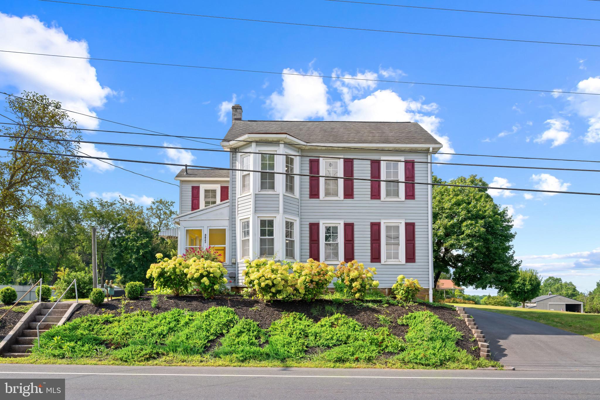 Stately Colonial home in desirable Littlestown, offering 2,954 square feet with 4 bedrooms, 3 full baths, 1 half bath, and an oversized 2-car attached garage—all set on nearly a full acre. Gorgeous landscaping, a retaining wall, and a long driveway that wraps around to the rear garage create an impressive first impression. From the main entrance, step into a sunlit foyer that opens to a welcoming open-concept family room with elegant chair rail detailing and a charming eat-in kitchen. The kitchen features additional breakfast bar seating, stainless steel appliances including double ovens, a bread cabinet, a mosaic tile backsplash, and abundant cabinetry and counter space. A nearby hallway houses well-appointed laundry facilities and offers exterior access to both sides of the property, as well as garage access. Continuing through the main level, the living room features architectural bay windows, a charming built-in corner bookcase, and a staircase to the upper level. Off the living room, a main-level carpeted bedroom with an attached full bath is ideal for guests or multigenerational living. Completing the main level, a 3 season porch is located off of the living room as well. Upstairs, you’ll find three sizable bedrooms and two full baths, including the expansive primary suite with a large walk-in closet and a private bath featuring a dual sink vanity. The lower level provides a blank canvas for your customization or excellent storage space.
Outdoors, enjoy a large side yard with a concrete patio, plus a level, fenced backyard that includes a second 2-car detached garage with a covered patio—perfect for entertaining or extra storage.