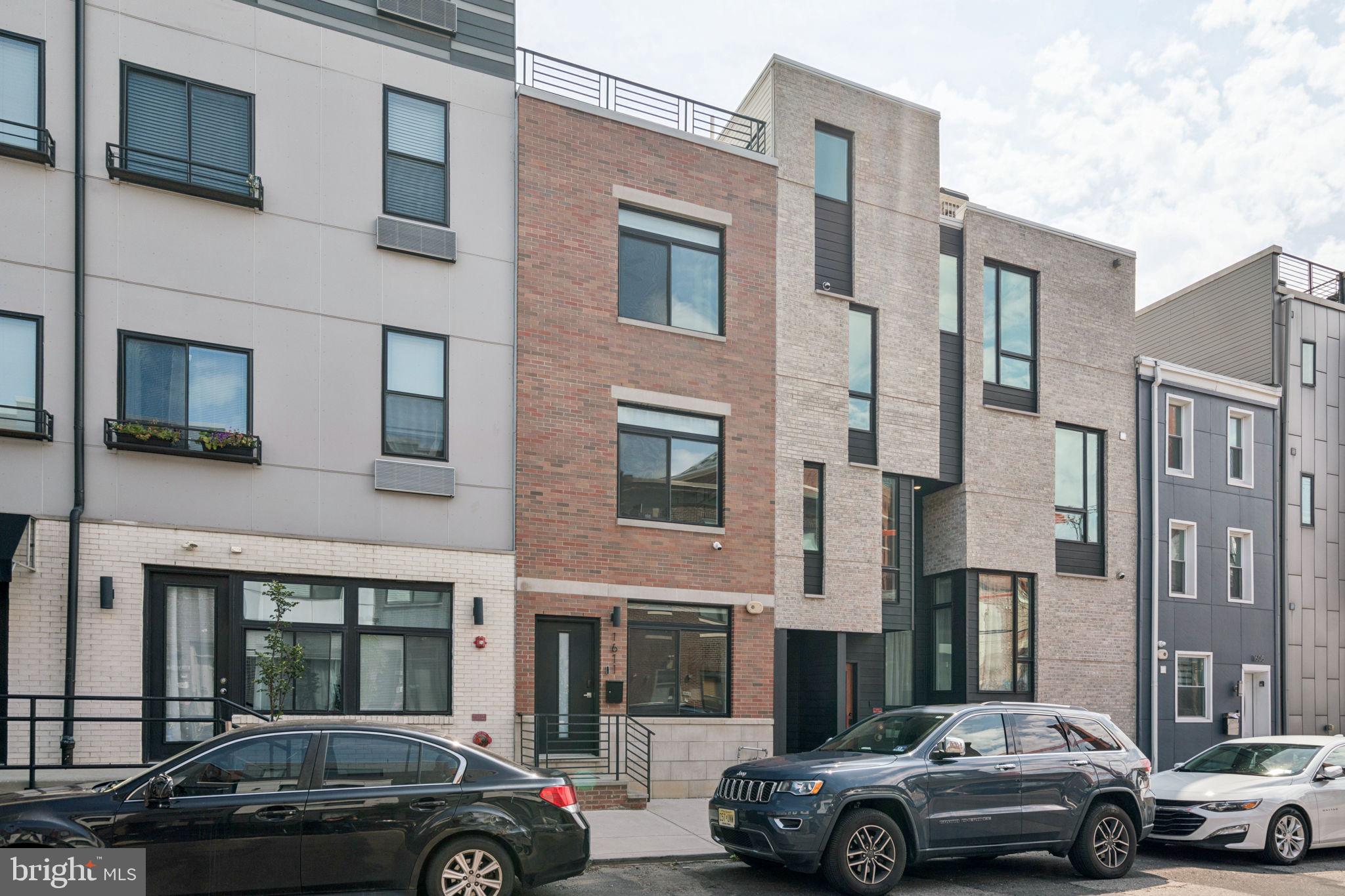 Welcome to 1611 Germantown Avenue — a beautifully maintained modern townhome built in 2021 and packed with thoughtful upgrades throughout. This 3-bedroom, 3.5-bath home includes a finished basement, a spacious rooftop deck with sweeping city views, and a full TAX ABATEMENT. The sleek brick façade offers curb appeal with a contemporary edge. Step inside to find wide-plank hardwood floors that run seamlessly throughout the home. The open main level offers plenty of room to relax or entertain, with space for both living and dining that flows into a chef’s kitchen at the rear of the home. The kitchen is outfitted with quartz countertops, stainless steel appliances, white shaker cabinetry, subway tile backsplash, and a large breakfast bar perfect for casual seating. Just off the kitchen, sits a stylish powder room. The second floor includes two bright and versatile bedrooms—ideal for guests or home offices—along with a full bathroom and a laundry room with built-in shelving. The third-floor primary suite is a true retreat. Before entering the bedroom, you’ll find a convenient wet bar with a mini fridge and cabinet space. The bedroom itself features excellent natural light as well as dual custom walk-in closets. The luxurious ensuite bathroom includes a dual wood vanity with backlit mirror, soaking tub, and a fully tiled glass shower with rainfall head and built-in niche. Walk up the steps and onto the expansive rooftop deck to take in panoramic skyline views — the perfect space for lounging or entertaining. Downstairs, the finished basement includes a full bath and can easily serve as a media room, gym, guest suite, or home office. Located in the heart of Olde Kensington, this home is just a short stroll to local cafes, shops, and restaurants. Don’t miss your chance to own this stylish, move-in-ready home in one of the city’s most vibrant neighborhoods.