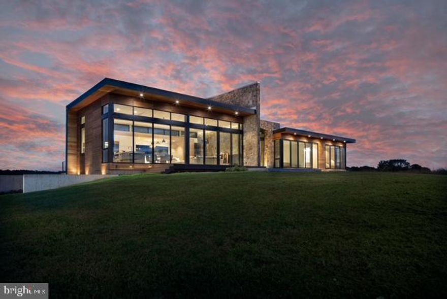 Amidst rolling hayfields and sweeping mountain views, House of Sky is a modern retreat designed for serenity and connection to nature. The striking stone-and-wood exterior opens to expansive western windows framing the Blue Ridge horizon. Designed by Lavinia Pasquina Fici and John Nahra, the home blends artistry with function in an exceptional 53-acre setting with hayfields, vineyard, and orchard.

Inside, the open kitchen/dining/living space soars with 15’ ceilings, bleached white oak floors, and walls of glass. Custom Cabico cabinetry, Brazilian granite, Caesarstone, and top appliances—Wolf, Sub-Zero, Bosch, and Grohe—make the kitchen a chef’s dream. Sliding doors lead to terraces for outdoor dining and entertaining.

The primary suite features floor-to-ceiling windows, a luxurious travertine bath with soaking tub, radiant heat, and spacious closet. A second bedroom with built-in bunks, private library, and lower-level wine cellar complete the home. Additional highlights include a garage, well-equipped laundry, and radiant floors.

Located just 5 minutes from Washington, VA, and 10 minutes from Sperryville, this extraordinary property offers modern design, peaceful solitude, and proximity to fine dining, boutique shops, and the best of Rappahannock living.