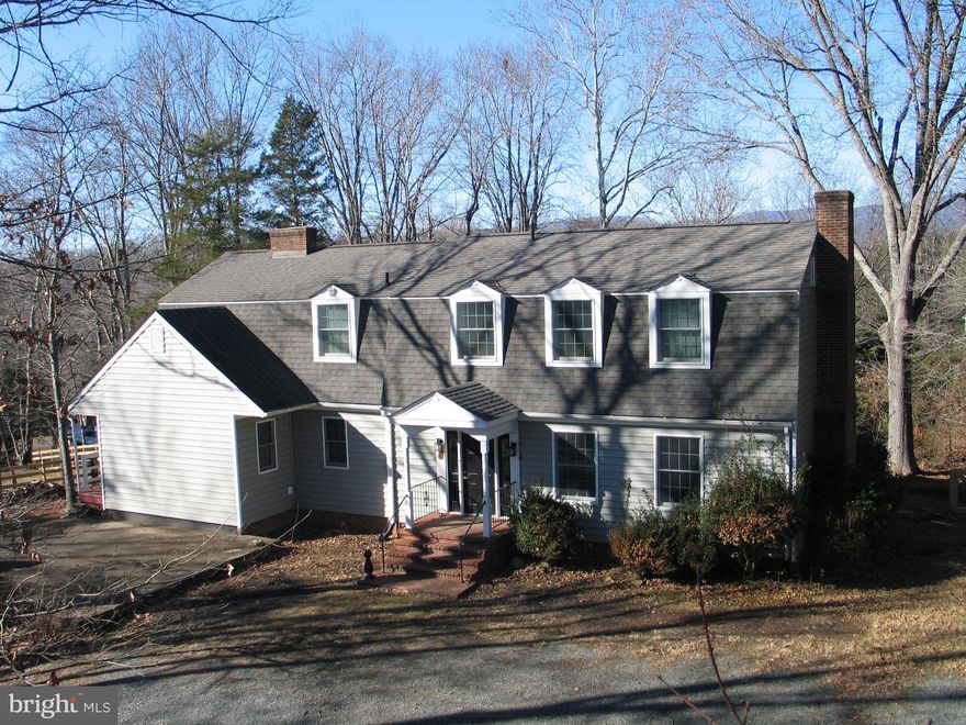 Take the 360 Walkthru Tour by clicking on the virtual tour link and explore the main and top floors just like you were there. As you wander through this unique Dutch Colonial style home you'll notice that it is not your standard house. Your eyes immediately drift to the wide-plank Heart Pine flooring throughout the first floor with chair railing and crown molding leading you from room to room. Turn right and go through the French Doors into the formal Living Room with the first wood-burning fireplace. Head towards the back and you'll catch your first glimpse of the Blue Ridge Mountains as seen from the rear windows of the home. Head through a second set of French Doors into to formal Dining Room. Perfect for entertaining guests while still drinking in the mountain view. Head thru the swinging door to Kitchen where you'll enjoy the abundant cabinet space, brick overhead accents along with the second fireplace shared with the open Den.  Take a quick step onto the back porch and deck for a breath of fresh air and the views then head back inside to imagine yourself enjoying your favorite beverage next to the fireplace with a few friends - someone else is cooking for you while still part of the conversation! When it's time for work continue through to the office/bonus room that features a side entrance from the left side covered porch. The laundry was moved to this level and is secretly placed here as a laundry closet. Finish the first floor in the hall headed back to the foyer and the stylish powder room. Hidden pantry shelves line the hallway behind the bifold doors. Head upstairs to the open landing and turn left into the owner's suite with your third fireplace. Use your imagination on the cool spring/fall nights or a winter snow. Continue around the corner to the owner's bathroom with walk-in closet, one of the largest soaking tubs on the market and step in, tiled shower.  Head back to the landing and continue to the left side of the house where you'll encounter the second full bath,  bedroom two with double windows and mountain views and finally the two-section 3rd bedroom.  The entry room would hold your furniture, seating area, etc and then walk around the corner to where you'd place the bed - fun layout!   Not in the virtual walkthru but no less important  is the basement. Block wall and concrete floors are great for storage and a workshop. There is a cedar closet in one section and a modest full bath (we call is three-quarters) perfect for washing down after gardening. The plumbing and wiring is still there for a 2nd laundry along with rough-ins for adding separate living quarters.  Walking out from the basement you'll find yourself in the fenced back yard. Continue out the side gate back to the front and you'll finish up at the concrete pad in the front which was placed to accommodate a garage or use it as an entertainment patio. Cooling is via a straight AC unit with plenty of ceiling fans to move air as well. The heat is via forced-air propane furnace or you can incorporate your 3 fireplaces into the mix. HVAC is old but still serving the home well. Make your way around the road bend to the community lake, shelter, beach and boat launch. Make sure to bring a kayak/canoe to enjoy the community lake and additional mountain skyline.