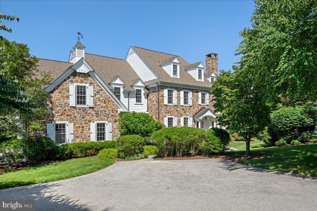 Tucked into the highly desirable Fenimore community in Gladwyne, this classic stone colonial—Built by Pohlig Builders, long respected for their superior craftsmanship and thoughtful design—offers timeless elegance and exceptional functionality. Set on Summerhill, a quiet cul-de-sac within the community that hosts just three additional homes, the property enjoys a private setting and access to the neighborhood’s open green space at the end of the street.
Finished across four beautifully executed levels, this home is designed to support both daily life and large-scale entertaining, balancing formal architecture with comfortable family living. A traditional center hall layout welcomes you with a gracious foyer flanked by a fireside living room on the right and a formal dining room on the left. Rich hardwood floors run throughout the main level, and the dining room connects seamlessly to a stylish butler’s pantry—open in design to lend a sense of flow between serving and gathering spaces.
The kitchen is expansive and light-filled, anchored by a large, seated island and appointed with high-end appliances. A charming breakfast room, wrapped in windows, opens to one of two stone terraces—this one outfitted with a built-in grill and generous seating area overlooking the mature rear landscape and century-old tree line. The kitchen flows into a large family room where a vaulted ceiling adds volume and natural light. A wood-burning fireplace, flanked by windows and custom built-ins, centers the space with warmth and architectural presence.
The mudroom wing provides a secondary entrance with utility and elegance—complete with a potting sink, a discreet home command center for managing household needs, and one of two powder rooms. This area also includes access to the oversized three-car garage. A richly paneled library sits just beyond the living room, offering a quiet retreat or sophisticated entertaining space with views of the rear grounds.
Upstairs, the primary suite is an airy, serene retreat. A vaulted ceiling adds light and dimension, while his-and-hers walk-in closets and a spacious dressing area lead to a well-appointed bath featuring dual vanities, a soaking tub tucked under a window with custom shelving, a separate seated shower, and private water closet. In addition to the primary suite, there are five family bedrooms on this level. One offers a private en suite bath and walk-in closet. Two bedrooms are joined by a Jack and Jill bath, while the remaining two share a thoughtfully designed connecting bath. All bedrooms are generously sized with either walk-in or double closets. A large laundry room completes this level with added convenience
A secondary staircase leads to the third level, where a bright office, large walk-in closet, and extensive storage await.
The finished lower level offers multiple areas for recreation and relaxation, including a fitness room, wine cellar, billiards space, TV lounge, and a full bath. Natural light filters in, enhancing the livability of the space.
Tucked just off the family room is a second, more secluded stone terrace—a hidden garden room of sorts. Surrounded by stone walls for privacy and shaded by a pergola with mature climbing vines, this intimate space is centered by a stunning outdoor fireplace—an ideal spot for quiet conversation or evening gatherings.
A rare offering in one of Gladwyne’s most sought-after neighborhoods, this home is at once refined and relaxed, grounded in classic design yet thoughtfully expanded for modern life.