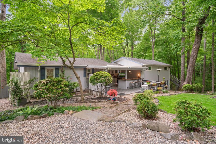 Welcome home to this stunning cabin, perfectly situated on a private 1.3 acre lot in the sought after mid-County community of Lake Jackson. The contemporary design seamlessly blends with rustic charm to create a truly exceptional home, featuring 4 bedrooms, 2.5 baths, and nearly 2,200 sq ft. Surrounded by mature trees and tranquil gardens, this property gives you a feeling of peace and serenity, yet minutes from award winning schools, commuter routes and shopping. The front porch is an entertainer's dream and a great place to gather with friends. Enjoy the firepit and watch the game from your very own outdoor bar! Step inside and you’ll be welcomed with old world charm with original wood floors and walls. The open concept living space highlights the natural beauty of the original cabin. The heart of the home is the updated kitchen, equipped with NEW stainless-steel appliances, sleek countertops, tin accent ceiling and ample storage space. The kitchen graciously opens to the family room, featuring vaulted ceilings, exposed beams and ship lapped walls evoking a sense of rustic charm. The wood-burning stove is surrounded by natural stone, providing both a focal point and a cozy spot to gather on chilly evenings. Expansive windows offer picturesque views, allowing abundant natural light to illuminate the interior and create a seamless connection with the outdoors. Watch the eagles sore from the covered back porch with beautifully exposed stone accent. The lower level features the expansive primary bedroom suite! This room has been designed with luxury and comfort in mind with barn doors accessing the walk-in closet with custom-built shelving. You will feel like royalty in the spa-like ensuite bath. Soak in the oversized tub after a long day, while catching up on your favorite shows on the wall-mounted TV. The wet room has stone flooring and is surrounded with rustic tile accents and a rain shower feature. This suite is complete with its own sitting room area with built-in flat screen tv and a private entrance. The lower level also has the 4th bedroom which makes for a great work out room, office, or man cave. Upstairs you will find the overly spacious second bedroom featuring vaulted ceilings, two closets, an office area, and a private deck with separate entrance! The full hall bath has been recently renovated with fresh paint, wainscoting and a sleek vanity. A cozy guest room with vaulted ceilings is also upstairs, next to a welcoming sitting room - perfect for snuggling up with a good book or converting to an additional office area. Have a hobby? This property includes an oversized workshop with custom built-in shelving and electricity! Additional parking near the workshop is available for your recreational fun. Enjoy boating, jet skiing, kayaking, fishing or simply going for a swim on a warm day! Lake Jackson is a private lake community with exclusive neighborhood access to several miles of waterway on the dammed portion of the Occoquan River. There is no HOA and a voluntary citizen’s association that gives you access to the famous ‘Big Beach’ and three boat ramps. Come live the lake life with all of this one-of-a-kind retreat while being able to easily commute to DC with the VRE Manassas Station less than 10 minutes away!