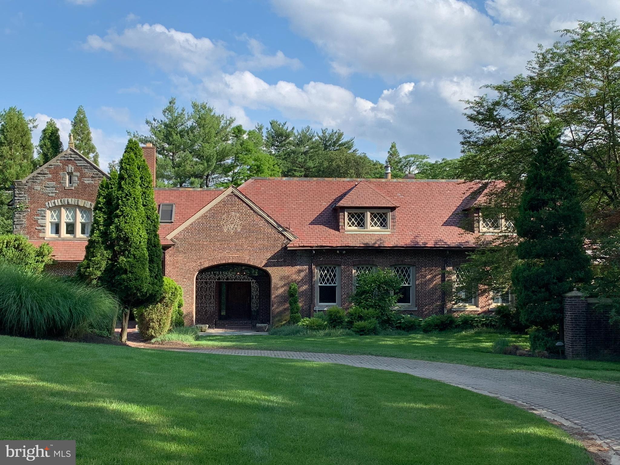 Situated on a manicured flag lot in Penn Valley, this exceptional 6-bedroom, 5.2-bathroom estate spans over 7,000 square feet of thoughtfully designed living space. Originally the carriage house to the magnificent Penshurst Estate built in 1901, this secluded retreat is accessed via a long, tree-lined drive. The culmination is a stunningly picturesque historic home with landscaped views of the home’s private 3-hole golf course and valley beyond.
An inviting front portico is a welcome entry into a grand hall, opening further to a splendid seating area with soaring ceilings and double doors that lead to a serene patio. High ceilings continue into a sophisticated library, where a mezzanine showcases curated artifacts. At the heart of the home is a majestic Great Room which includes breathtaking 30+ foot ceilings, exposed beams and exotic rattan, beautifully incorporating elements of the home’s historic carriage house pedigree. The space opens directly to the pool, slate stone terrace, golf course and views beyond, creating an effortless indoor-outdoor lifestyle.
Designed for both entertaining and everyday living, the kitchen offers a premier cook’s environment and features a generous center island, stainless steel appliances, tiled flooring, exposed brick, and expansive windows that flood the space with natural light. The kitchen flows seamlessly into the cathedral ceiling family room, beyond which lies an elegant passageway leading to a guest suite comprising a sitting room, guest bedroom, and full bath. A cast iron spiral staircase from the guest suite descends to a large versatile lower level. Complete with a half-bath and kitchenette. The space can be used as an office, gym, or family entertainment room. French doors lead to a covered exterior entrance and stairwell offering desirable private use.
An original carriage door at the East side of the family room leads directly into a distinctive music area of the Great Room, where diamond paned glass windows and exposed stone add warmth and character to the space. Set back from the common areas is the home’s primary suite. It is an impressive sanctuary featuring an oversized walk-in closet, an ensuite bathroom with separate vanities, a glass-enclosed standing shower, soaking tub, and dramatic arched windows. Across the way, a dressing room and day bed with a full bath provides the perfect multifunctional space. Additional first-level conveniences include a powder room, laundry room, and mudroom. The second level offers bright and airy bedrooms plus a full hall bathroom with dual vanities, a soaking tub, and a glass-enclosed shower illuminated by skylights. An additional in-law or au pair suite, complete with a kitchen, full bathroom, seating area, and a private entrance, ensures flexibility for multi-generational living.
Completing this extraordinary property is a well-appointed mudroom, a security system, a generator and a one-car garage with EV charger and additional turn around area for parking. For a unique touch of luxury, a professionally installed three-hole golf course sits adjacent to the house. The property is close to shops, parks, restaurants and is a ten-minute drive to Suburban Square. Furthermore, the house is located in the award-winning Lower Merion School District, boasting Penn Valley Elementary and Welsh Valley Middle School in close proximity. The Penshurst carriage house offers the rare combination of masterfully appointed historic space in a setting of unparalleled elegance. This exceptional residence is a true private oasis, combining refinement, comfort, and unique architectural elements with a warmth and comfort that exemplifies home.