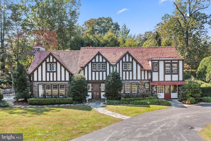 Imagine winding up the private cul-de-sac past graceful trees dotting the two acres to the stone gatehouse. Into view come orderly gardens, stone walls with arched doorways, and English Tutor structures that welcome you like a warm embrace. There is a sense of community, but the vision line from the house is private. 
You walk into your home and the hall’s burnished wood exudes both history and comfort. The living room, stately with a French marble fireplace, multi-paned windows, and two sets of French doors leading to the terrace, invites gatherings. The dining room is elegant and dignified, with wainscoting, crown molding, and deep windows. One can almost hear the tinkling of crystal, the laughter of family and friends.  
The den, wood-lined and bay windowed, is a cozy refuge. On winter nights the fire crackles. A secret room behind the bookcase, once the gatekeeper’s watch place, now serves as a bar. The kitchen, with reclaimed yellow pine from the stables, a wall of windows, and copper-edged counters, has an island with gas grill and stovetop.
Ascend the staircase to the master bedroom, which has shades of restful white on white, damask walls, French doors and balcony, marble fireplace, and a window alcove perfect for quiet solitude. 

The airy upstairs office has inset-wood shelving and desks and a view of the estate. The bedrooms are comfortable, tasteful. The basement is a hobbyist’s dream. 

Once the gatehouse to the mansion of Lily Busch of Anheuser-Busch fame, it is a home with heritage and character, sophisticated and livable.