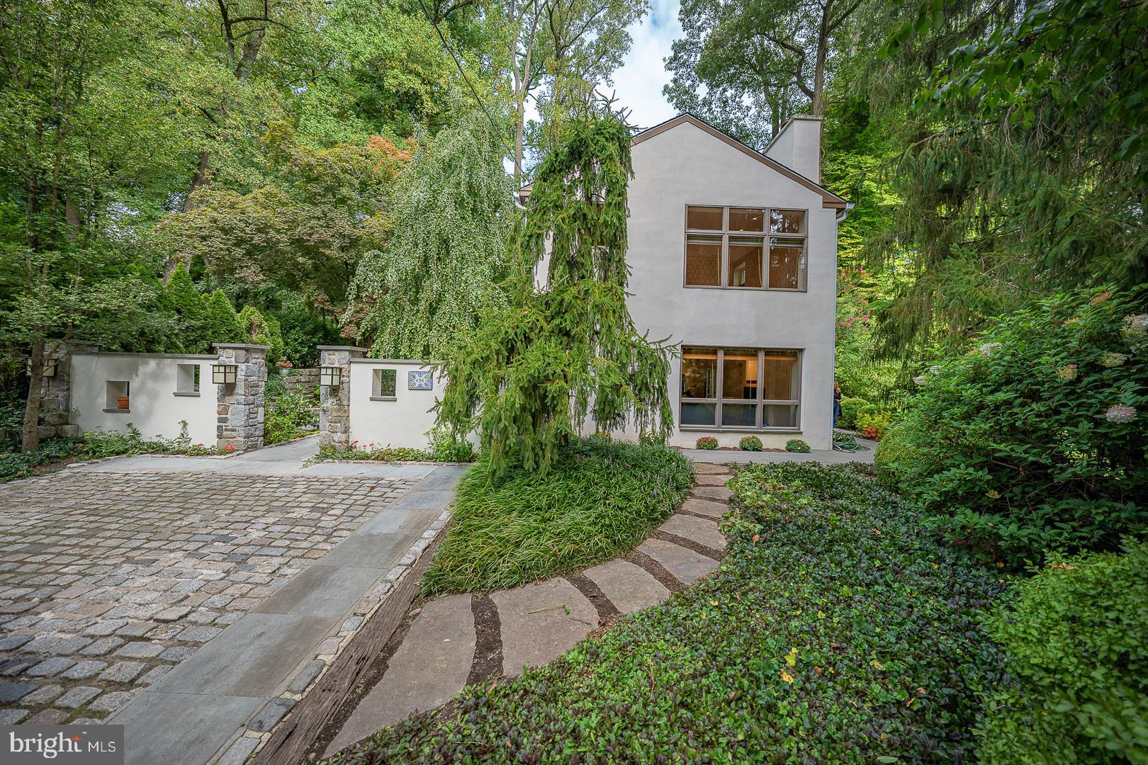 Set atop a gentle hill back from the road you will find this enchanting Northside Bryn Mawr carriage house which was completely renovated in 2015. Originally a carriage house and separate stable this special property has been combined and renovated to be one living space surrounded by European gardens designed by landscape architect Gordon Eadie, 3 terraces and a grand flagstone courtyard embraced by an 8 foot retaining wall This courtyard creates a private peaceful area to enjoy morning coffee or host a gathering and is the main entrance to the home. As you enter the home you will be struck by the sun filled open space where the living and dining areas are both open to the beautiful kitchen with island seating. Beautiful wide plank cherry floors with radiant heat and a wood burning fireplace with gas starter provide a warmth to this heart of the home. French doors lead to one of the three terraces where you can soak in the sun and natural setting. To the rear of the home find a special unique space perfect for an au pair/in law/office or guest quarters which includes a bedroom, full bath, and living area with its own private flagstone terrace. This charming space is connected to the main carriage home but also has its own entrance. Cherry flooring continues up the staircase and throughout the second floor where you will find a spacious primary suite with soaring ceilings, a bath with radiant heated floors, dual sinks, walk in shower with multiple heads and a large walk in closet. A second bedroom suite with full bath and a separate convenient laundry room completes this level. Enjoy the private setting and scenic views out each window. This low maintenance special home is a wonderful alternative to townhome/condo living located in the heart of the Main Line- close to the train, shops, and restaurants. You must see it to appreciate all it has to offer!