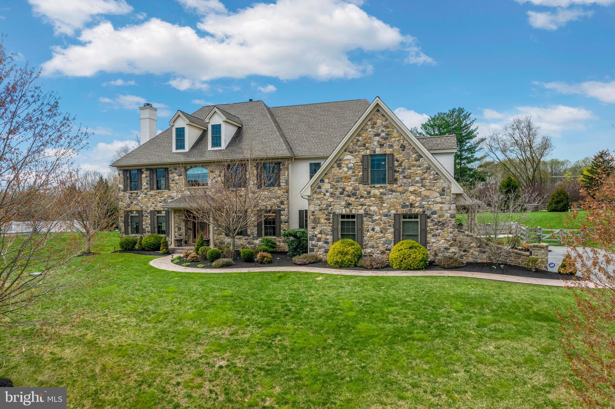 Welcome to this sophisticated custom home in the desirable Parker Preserve Community located in the award-winning Unionville-Chadds Ford School District. The Parker Preserve Community is tucked into the Chester County countryside, yet conveniently located to all the area restaurants and attractions.
The inviting landscaping with perfectly placed plantings and stamped concrete path showcase the home’s natural stone façade. This five bedroom, six full and two half-bath Colonial style home features abundant living space and high end finishes. Enter through the front entry door into the foyer highlighted by a luxurious staircase and gleaming hardwood floors. Both the formal living and dining rooms feature upgraded trim packages including wainscoting, crown molding, and a tray ceiling in the accent dining room. The formal living includes one of four fireplaces located throughout the home. Just off the formal living room is a large home office with built-ins and easy access to the elegant guest powder room. Behind the office is the sunroom that lives up to its name and it the perfect setting for your morning coffee. The hardwood floors continue into the kitchen which features antique white cabinetry, oversized center island and granite counter tops. The appliances are a chef’s dream and features a Wolf eight burner cooktop, pot-filler, a spacious Subzero refrigerator, two Bosch dishwashers and dual Wolf wall ovens. For additional entertaining and storage space, off the kitchen area are two butler pantries with one wine cooler and a walk-in pantry. The eat-in kitchen area opens to the spacious family room with wood burning fireplace and coffered ceiling. Proceed upstairs where you will find that the hardwood floor continues into five generous bedrooms, all featuring their own en-suite bathrooms and walk-in closets. The second-floor spacious landing balcony leads to double doors which enter into a grand luxury main bedroom. The luxurious main bedroom is accented by the tray ceiling and kept warm by the gas fireplace. The main bathroom provides two over-sized vanities, a separate water closet, as well as a soaker tub and large tiled shower. A roomy second floor laundry includes a utility sink and quality cabinetry. The airy, walkout finished basement is anchored by the custom wet bar with granite counters, dishwasher and wine cooler. The area also includes tiled floor, an additional gas fireplace and a full bathroom. An additional work area/guest bedroom and media room complete this home. Additional features include a maintenance free deck, Pella windows throughout, Nest thermostats, whole house water softener and humidifier, fenced in backyard, central vacuum and home security system. Each design selection was carefully considered to create a nearly perfect home experience.