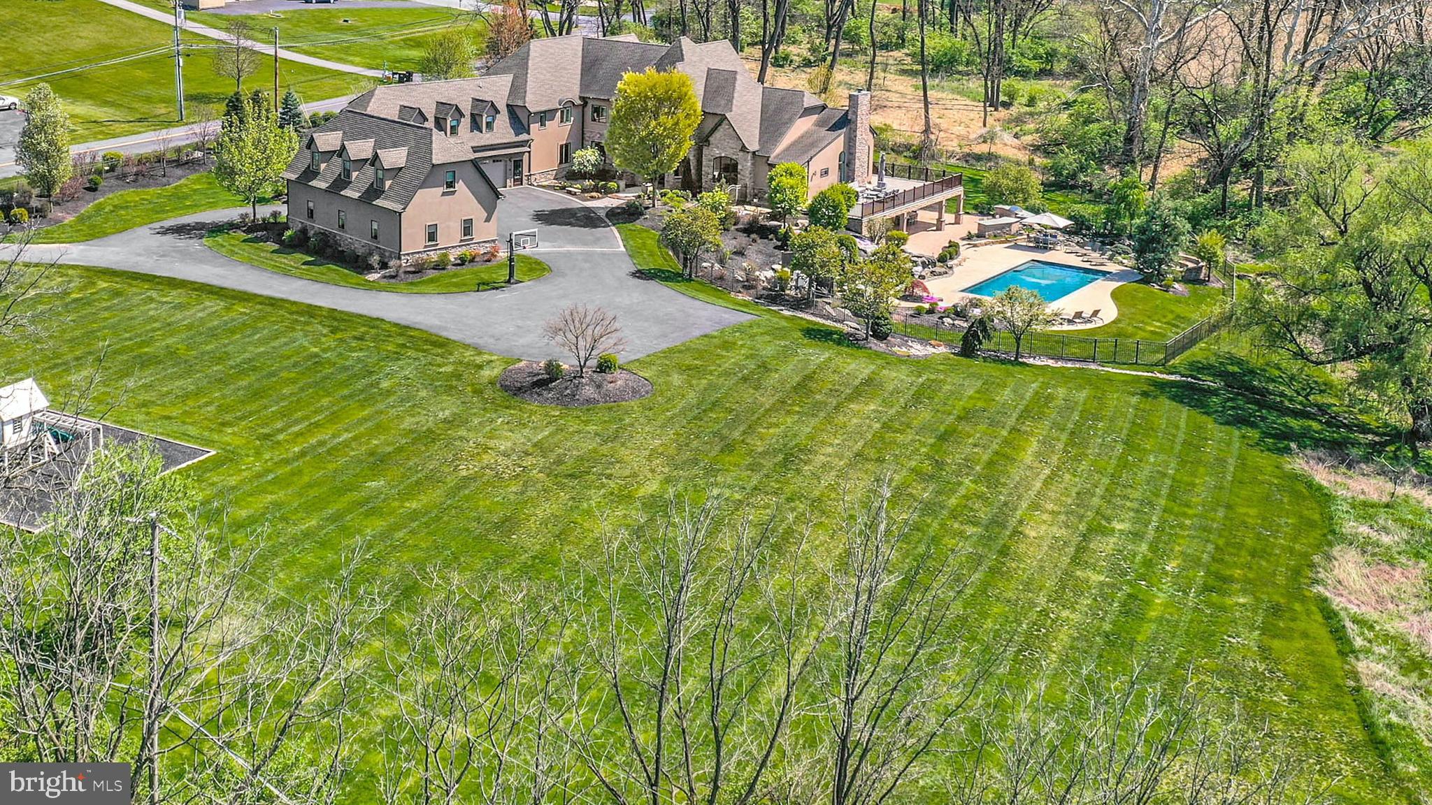 Welcoming…gracious…refined. Hidden Gem is a work of art, showcasing classic architectural elements, world-class materials, modern technology, and superb craftsmanship, nestled quietly in a lovely backdrop with hills and meadows beyond. Custom built with more than 14,000 square feet of finished living space over 3 levels along with a multitude of outdoor amenities, this is truly a home for all seasons of life.
Inside, each room is bathed with light in a layout that showcases high ceilings, hardwood floors, & plentiful custom built-ins. The gated entry & circular driveway lead to a 2-story covered porch with stone columns. Double doors open to the foyer, boasting a heated travertine floor, sweeping staircase, 2-story ceiling with custom crystal chandelier, & reclaimed barn beams framing a hand-painted mural by artist R.J. Buckingham. An arched opening leads to the large dining room and 2.5 story great room beyond, with more locally reclaimed beams, a floor-to-ceiling fireplace & custom entertainment center. The gourmet kitchen boasts every appliance required by a master chef, with a plethora of soft-close mahogany cabinets & both honed & river rock granite work surfaces. Nearby, a walk-in pantry is outfitted with matching custom cabinets & counters, while the breakfast room looks out over the private back yard. A large family room provides space for relaxing, while the adjacent satellite kitchen offers additional cooking & prep space. More custom built-ins can be found in the office, and a large 1st fl laundry room includes 2 sets of washers and dryers. A custom designed mudroom includes a walk-in coat closet large enough to accommodate outwear for every season, & leads to the attached 3-car garage. 2 large bedroom suites are on this level as well, each with a walk-in closet and custom en suite bath. Front & back stairs lead to the 2nd floor, with an elevator servicing all 3 levels of the home.
The primary suite features a private balcony, unique ceiling lights & romantic gas fireplace with marble surround. Multiple walk-in closets include custom storage, built-in shoe racks & vanity station. The luxurious private bath includes radiant heated floors, an air-jet tub, glass walled shower & vanity with dual sinks. 2 more generously sized bedroom suites are on the 2nd floor, each offering a unique aesthetic, with custom en suite baths & walk-in closets. A guest or in-law suite with separate outside entrance offers a full bath, living area & kitchenette.
Visitors will feel as though they have been whisked away to a 5-star resort in the elaborate walkout lower level. A home theater with tiered seating & state of the art projection system offers family night fun, with an adjacent movie theater-style snack counter & kitchenette. The recreation room with radiant heated floor is open to the large wet bar. A full size exercise room is an unexpected amenity, & the adjacent bathroom with steam shower is a perfect post-workout treat. Office space, an additional full bath, & multiple storage rooms are on this level as well. Glass doors lead to the multi-level outdoor space, where a partially covered paver patio includes an outdoor kitchen with built-in gas grill, outdoor speakers, ceiling fans & TV hookup for impromptu dinner parties. The heated in-ground pool has concrete decking & a separate spa surrounded by natural rock features. A koi pond, stone waterfall, and built-in gas fire pit are ideal for whiling away afternoons and evenings in every kind of weather. Along with the 3-car attached garage, there is a separate detached 3-car garage with a fully floored second level, plumbed for heat and a full bath. A whole-house generator brings peace of mind year round.