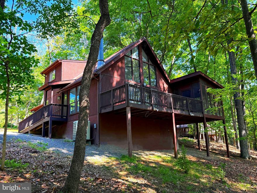 Tucked among nearly two wooded acres in a sought-after golf resort community, this contemporary style cabin offers the perfect blend of comfort, style, and resort living. With 3 bedrooms, 2 full bathrooms, and 1,456 square feet of finished living space, this home is designed to feel both spacious and welcoming.
Inside, gorgeous LVP and hardwood flooring flow throughout the home, while a dramatic cathedral window fills the living room with natural light. A wood-burning stove adds warmth and ambiance, creating the ideal gathering space year-round. The main level features two generously sized bedrooms, while the upper level offers a private retreat complete with a spacious bedroom, full bath, and walk-in closet. The updated kitchen is beautifully appointed with new cabinetry, granite countertops, and stainless steel appliances, combining modern convenience with timeless appeal. Just off the family room, the screened-in sunroom provides a peaceful space to relax and enjoy the surrounding nature in every season. An adjoining open deck is perfect for grilling, outdoor dining, or simply taking in the wooded setting. Outside, the large gravel driveway and parking area offer ample space for guests and multiple vehicles. Optional resort membership packages provide access to an impressive array of amenities, including an 18-hole golf course, Clubhouse Grille & Pub, indoor and outdoor pools, tennis and pickleball courts, a sports center with basketball and volleyball courts, catch-and-release fishing ponds, and spa and wellness services at Sleepy Creek Spa. Conveniently located just 90 minutes from the D.C./Baltimore metro area and only a short drive to Berkeley Springs, this property offers the ideal escape for full-time living or a relaxing weekend retreat.