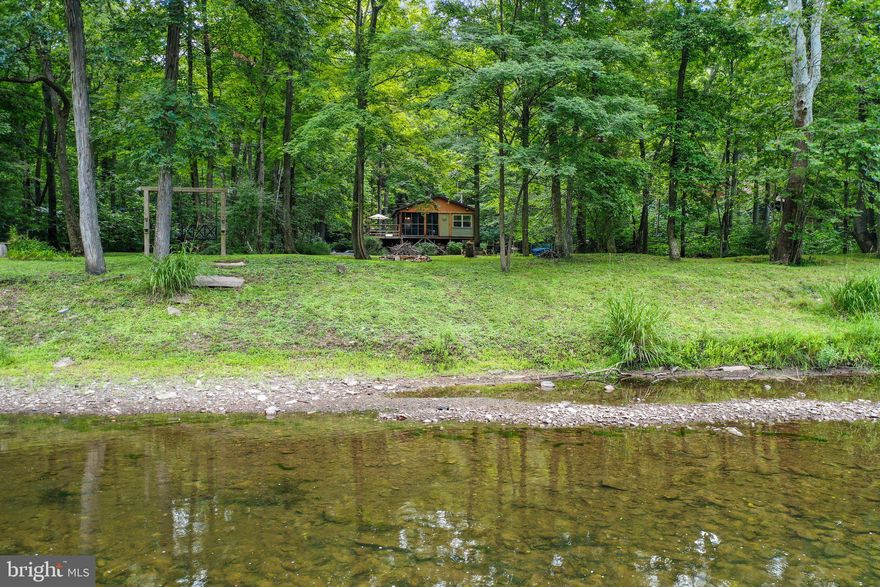 Amazing CACAPON RIVER waterfront cabin. Featuring an open floor plan with a kitchen, great room with cathedral ceilings, and a wood stove, access to the screened in porch, a barn door leading to one of the two bedrooms.  Outside you'll have 190.78 ft of riverfront, with a park like setting, with evergreen trees and lots of flower, an outside shower, from the house are pavers leading to the river, 2 fire pits and a shed with electricity.  You can go swimming, tubing, kayaking, canoeing, or go fishing. Relax by the firepit while listening to the sound of the river or look for eagles, blue herons, turtles, crawfish, fox and deer.  Lots of care has gone into this move in ready cabin.   Here is a list of some of the improvements:  new plumbing, mini split unit for heating and air conditioning, new wiring, all new post and footers, new kitchen cabinets, new kitchen and great room flooring, new rugs, new woodstove and SS piping, whole house insulation, new windows, new patio, gutter guards and a new concrete foundation. This move in ready home is in the flood plain.  The Seller will pay the first year of flood insurance up to $1,000.00.  Please review the estimate I have provided.  This is a must see when looking for that get-away home. Airbnb okay!