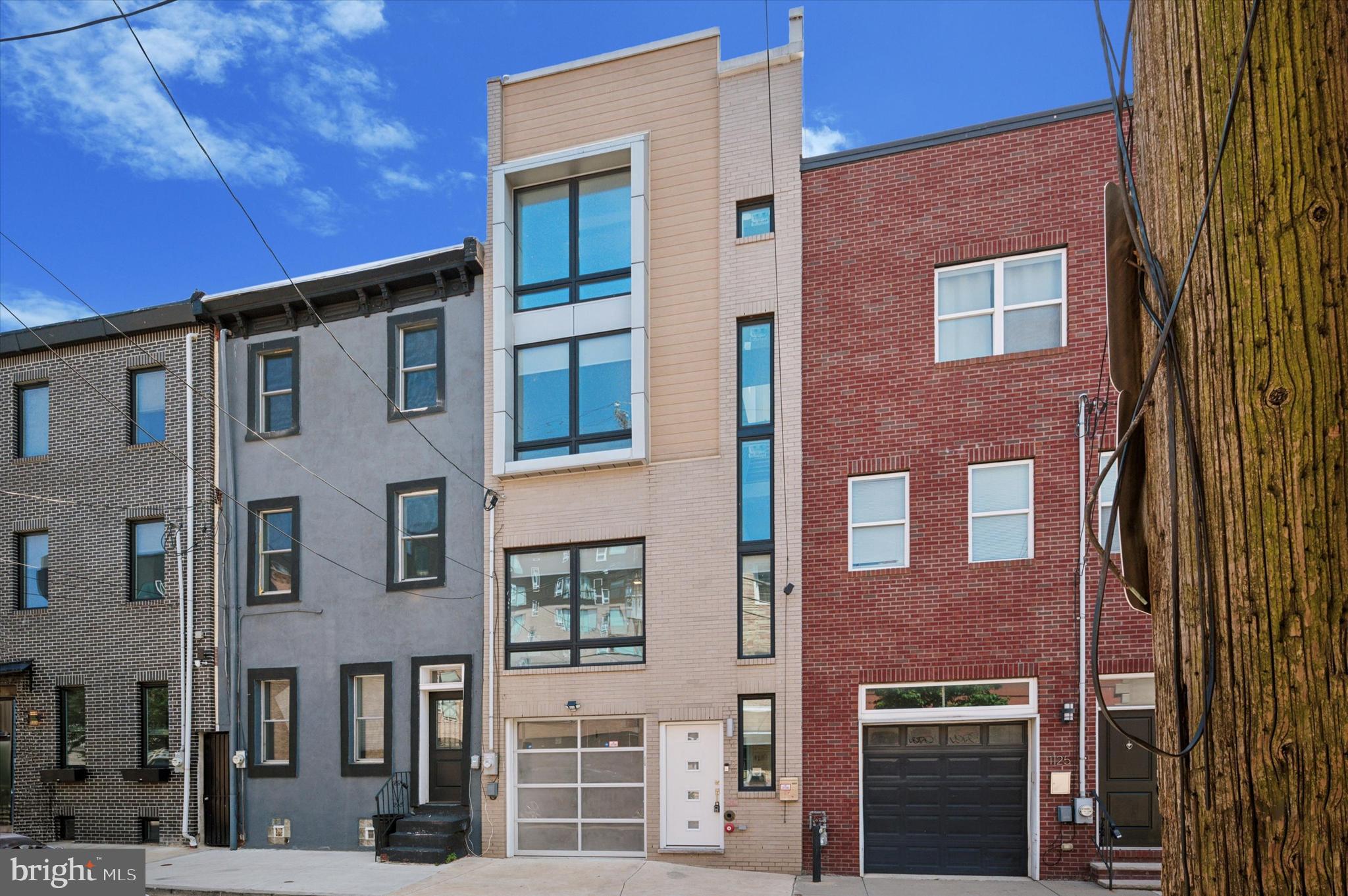 Welcome to your stunning new home at 1127 Leopard St, perfectly situated in a prime location! This custom-built residence spans four stories and boasts impressive features, including 11-foot ceilings on the second floor and 8.5-foot ceilings on all other levels. The modern exterior showcases a stylish combination of gray modular bricks, complemented by Ipe wood tiles and contemporary aluminum accent panels around the windows on the third and fourth floors. Parking is a breeze with an attached garage featuring sleek modern tempered and translucent glass panels and aluminum framing. Natural light floods the interior through large floor-to-ceiling windows, three skylight wells, and additional side windows on every floor, all equipped with triple-pane glass for superior noise reduction and energy efficiency. An open foyer extends from the first floor to the roof skylight well, creating a bright and welcoming entrance. Throughout the home, you'll find elegant modern French gray 6-inch wide engineered hardwood floors and freshly painted. Enjoy optimal comfort with a high-efficiency two-zone Fujitsu mini-split/ductless HVAC system with eight individually controlled blowers and universal remotes. Every staircase is enhanced with metal railings on both sides for added safety and style. The home also features the maximum R-values for insulation at the time of construction, ensuring energy efficiency. The ground floor offers a versatile room ideal for a home office, gym, or den, along with a convenient powder room, and opens to a private rear concrete patio with an engineered wood fence via double glass French doors with built-in blinds. The second floor presents a complete open concept layout, featuring a modern/minimalist kitchen system by Pedini imported from Italy, complete with a motorized overhead wall cabinet, push-open soft-close wall cabinets, a stainless-steel backsplash, built-in KitchenAid appliances (counter-depth fridge, induction cooktop), a hidden hood, EKO Collection cabinets, a white Betacryl countertop, a White Oak Lacquered Wood peninsula table, and a kitchen island with a Betacryl countertop and sink, a built-in Summit beverage cooler, and a Miele dishwasher with garbage disposal. The living room boasts floating TV entertainment cabinets with matching Betacryl worktops and a modern stainless steel ethanol-fueled fireplace. The third floor includes two generous bedrooms and a full bathroom, with the rear bedroom offering access to a private balcony via a double glass French door with built-in blinds. The entire fourth floor is dedicated to the luxurious master suite, featuring two skylight openings, a reach-in closet, and a spacious walk-in closet with a custom California Closets system. The spa-like master bathroom includes a custom shower pan with a prism glass enclosure and door, a high-end stainless steel multi-functional shower jet panel, a wall-mounted waterproof touchscreen for steamer control, and a state-of-the-art oval whirlpool jet tub. Outside access to your rooftop deck with views of the Philadelphia skyline. Plus, with five years remaining on a 10-year tax abatement, you'll enjoy significant savings for years to come.