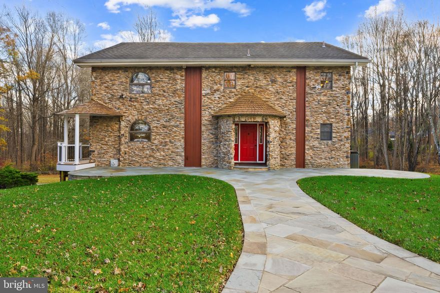 Distinctive contemporary stone Colonial set on over three private, wooded acres in Foxhall Villas. Its exterior makes a memorable first impression with a full stone façade accented by vertical architectural details that balance timeless craftsmanship and modern design. A long, curved flagstone pathway and front patio lead to a striking red front door framed by a rounded stone entryway. Inside, premium Brazilian cherry hardwood floors flow throughout a bright, open, and airy layout. The design blends modern and vintage influences with warm neutral tones, earthy textures, and an abundance of natural light from oversized windows.

The foyer offers three closets, including one walk-in, and a convenient powder room. To the right of the staircase, the spacious family room enjoys ample sunlight and comfortable gathering space. Continue into the open-concept great room, where a sunlit living area features a built-in bench seat, soaring ceilings, and dramatic stacked windows. The adjacent formal dining room showcases a vintage-inspired chandelier, exterior access, and an open cutout shelving wall for decorative display or additional storage. Beyond the accent wall lies the gourmet eat-in kitchen, featuring a large island with breakfast bar seating and a floating sink illuminated by statement pendant lighting. Highlights include stainless steel appliances, granite countertops, a warm backsplash, ample cabinetry, a writing station, a butler’s pantry, and additional exterior access for easy indoor-outdoor flow.

Upstairs, the loft/sitting room features vaulted coffered ceilings and a centrally located laundry closet. Three bedrooms and three full bathrooms complete this level, including a remarkable owner’s suite with vaulted ceilings accented by exposed beams, a spacious walk-in closet, and a stunning bathroom with vibrant tilework, a soaking tub, dual sinks, and a separate shower. A second bedroom also includes a private bath and walk-in closet, while the third bedroom offers double closets and vaulted ceilings with exposed beams. The uppermost level loft includes a bonus room ideal for a home office overlooking the owner’s suite, an additional loft space perfect for a playroom, and a utility room.

The fully finished walk-out lower level expands the living space with a recreation area, a carpeted sitting area, a dining space, and a second full kitchen with stainless steel appliances. This level also includes a laundry room, a fourth bedroom, and a full bathroom. Outdoor living is a true highlight, with a two-tiered wraparound composite deck overlooking the tranquil, wooded backyard—private, peaceful, and perfect for relaxing or entertaining amid nature’s beauty.