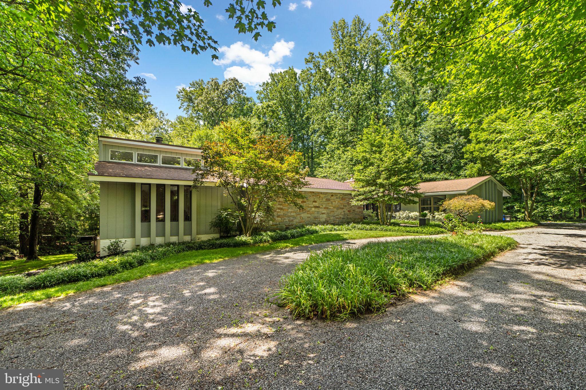 Welcome to a truly one-of-a-kind custom rancher offering 5,967 total square feet of living space, beautifully nestled on 2 peaceful, wooded acres in the heart of West Friendship. Enveloped by mature trees and natural beauty, this striking residence showcases distinctive architecture and retro-inspired design with mid-century flair. Inside, you'll find expansive living spaces, clean lines, and thoughtfully curated details throughout, offering a rare opportunity for those who value bold style, privacy, and timeless character in a breathtaking setting.A beautifully landscaped front courtyard welcomes you inside the foyer, opening to a bright, spacious living room framed by elegant columns and featuring hardwood floors, a striking brick accent wall with a wood‑burning fireplace, skylights, and expansive windows. A sliding glass door leads to the outdoor living area, creating a seamless flow between indoor and outdoor spaces. The formal dining room is adorned with hardwood floors, a modern chandelier, two unique wall cut‑outs, and a crisp white brick accent wall. An adjacent sunroom offers panoramic views of the lush surroundings, enhanced by soaring vaulted ceilings and sliding glass doors that open to the deck. The eat‑in kitchen shines with stainless steel appliances, ample cabinetry, elegant gold accents, and a large skylight. A breakfast bar framed by a wainscoting‑accented wall provides a convenient pass‑through view of the family room, while an adjacent breakfast area offers easy access to the outdoors and the garage. The inviting family room showcases a second wood‑burning fireplace with a natural wood mantel, complemented by an accent wall that adds character.The luxurious primary suite is a serene retreat with vaulted ceilings, skylights, and track lighting that fill the space with natural light. It also includes access to a private balcony and a double‑sided gas fireplace that connects the bedroom to a cozy sitting area. The spa‑inspired primary bathroom features a spacious corner vanity, a jetted tub, a walk‑in steam shower, and a private sauna. A separate dressing room offers a built‑in vanity with a sink, a walk-in closet, and a bench for added convenience. The main level also includes two additional spacious bedrooms with hardwood flooring and a second full bathroom. The finished lower level offers a comfortable recreation room with plush carpeting, a wood‑burning fireplace with a white stone surround, a second kitchen, and a full bathroom. A bonus area with LVT flooring and walk‑out access makes an ideal space for a home gym, while another versatile room can be used as a fourth bedroom. Outdoors, the private backyard is a tranquil escape surrounded by mature trees. Enjoy a deck with a wraparound built‑in bench and flower planters, a covered patio, a chicken coop, and a storage shed.