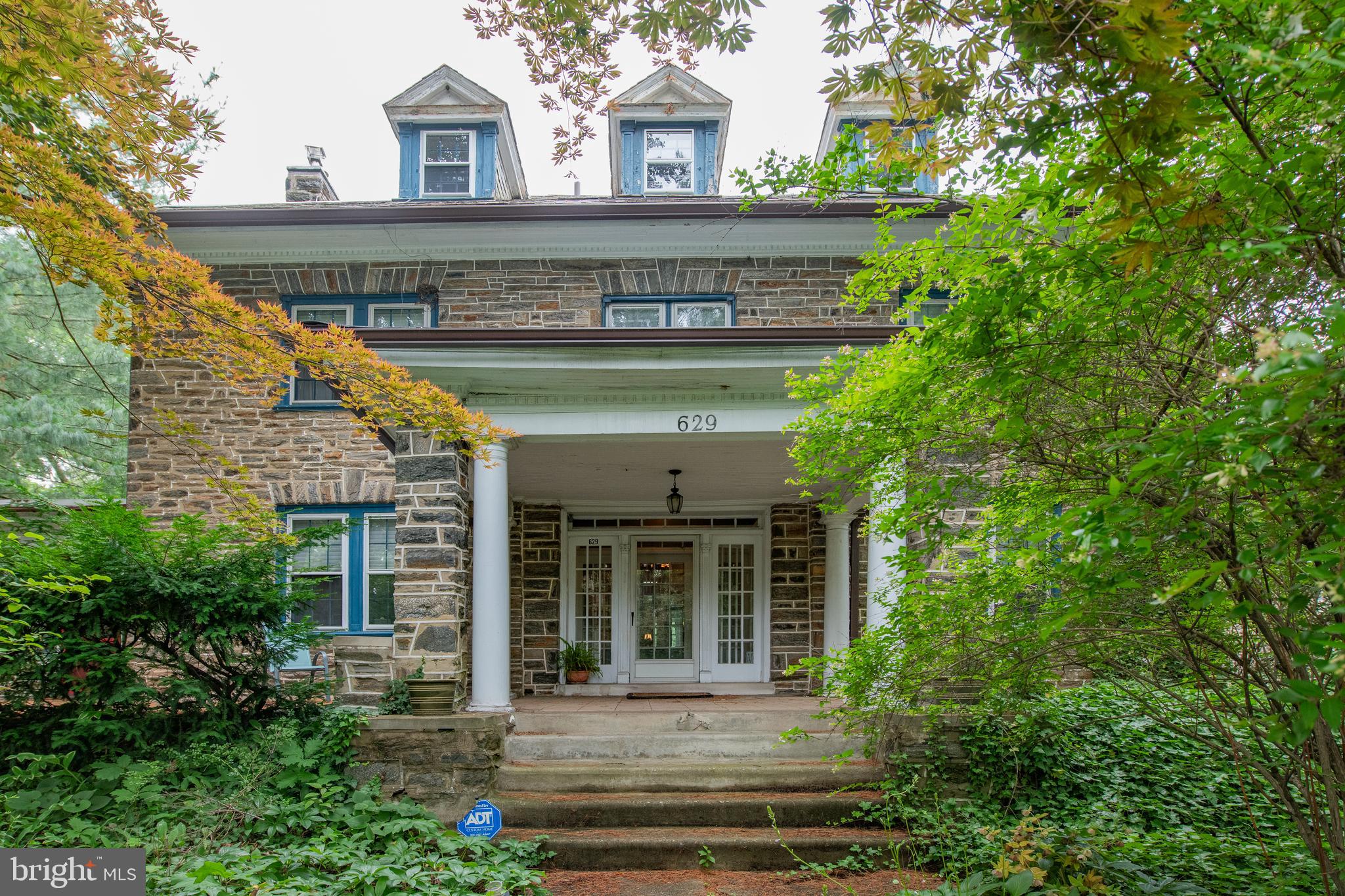 Elegant 1920s Stone Colonial in the heart of West Mt. Airy! Step into timeless charm and modern comfort in this grand colonial, located on a picturesque street just moments from the Wissahickon trails, Weavers Way Co-op, High Point Café, historic RittenhouseTown, and the regional rail to Center City. With Lincoln Drive only minutes away, you'll enjoy seamless access to both urban life and nature’s retreat. Lovingly maintained and thoughtfully upgraded by generations of owners, this stately 6-bedroom, 3.5-bath home offers a blend of gracious spaces and cozy nooks, perfect for both entertaining and everyday living. Original wood floors flow throughout, enhancing the home’s historic character. Here is the floorplan: Enter into a quintessential Mt. Airy foyer that sets the tone for this elegant home. To the left, you'll find a spacious formal living room featuring recessed lighting, custom built-in bookcases, abundant natural light, and a decorative fireplace. Continue through to a sunroom wrapped in three walls of windows, providing a serene view of lush greenery—a perfect space for reading, relaxing, or indoor plants. Off the foyer is a versatile bonus room—ideal as a hobby space, mudroom, or gardener’s nook! On the right, the formal dining room includes a privacy door that leads into the expansive chef’s kitchen. This kitchen is a cook’s dream with ample counter space and cabinetry, a center island with gas cooktop, double wall ovens, a second sink and dishwasher for prep, and easy access to the backyard. Laundry room is just off the kitchen. Up the main staircase, a wide landing features charming built-in window seating. Four generously sized bedrooms and two full baths provide flexibility and comfort. Three of the bedrooms connect, allowing for a truly exceptional primary suite complete with sitting room, dressing area, office, or nursery. The third floor adds two more spacious bedrooms and a full bath—ideal for guests, creative workspaces, or multi-generational living. Exterior & Extras: The landscaped front yard is filled with mature trees and indigenous plantings, creating year-round natural beauty, shade, greenery and privacy. A detached driveway leads to a stone garage, with finished exterior matching the main home. Above the garage, there's potential to create an additional studio, home office, or guest suite—bring your vision! Notably, the current owners have invested over $50K in preserving the original slate roof, ensuring lasting quality and historic integrity. This is more than a house—it’s a story, a sanctuary, and a rare opportunity to own a piece of Mt. Airy history