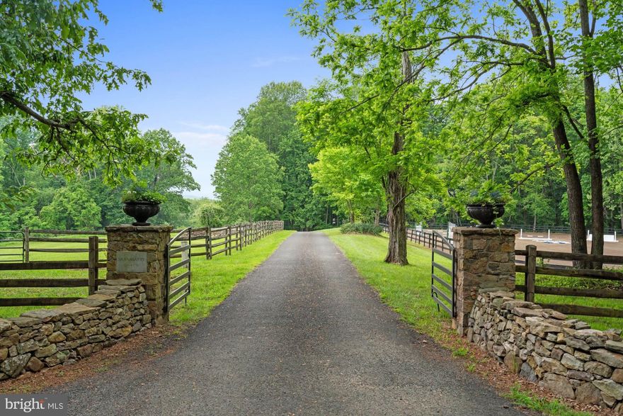 Shanagarry Farm on more than 51 acres is available for the first time in nearly four decades. A bucolic estate near the foothills of the majestic Blue Ridge mountains in Castleton, Virginia just 15 minutes from Warrenton. Shanagarry means “old garden” in Gaelic and these gardens certainly deliver on the name. They’re full of rare, antique varieties of roses and heritage plants surrounded by 150 year old boxwoods highlighted by tiered flagstone terraces with a salvaged millstone inlayed within the entrance courtyard. The four bedroom farmhouse dates back to the 18th century. In fact, letters written in quill pen were discovered in the walls and date back as far as 1792. Much of this family home embraces the elegant history with original wide floorboards in the formal dining and living room including an antique wood burning stove. The warmth and character is carried throughout two levels with reclaimed floors and beams, a pantry door from the former Gold Cup course and a barn stall door used as an interior wall. It’s a home of tranquility and splendor where every corner whispers tales of timeless charm and boundless potential. The bright kitchen featuring lacquered wood countertops and a new Viking range opens to a double height eat-in sunroom with views of the rear grounds, covered stone terrace with pizza oven and dazzling views of a nearly one acre pond stocked with Bass, Catfish and others along with incredible birdlife. The oversized family room is designed for entertaining and features a custom wet bar with backlit bottle storage and two wine refrigerators. You’ll find two more bedrooms in the 1800’s chestnut log cabin straight out a storybook which captures the essence of rustic elegance. It was originally built just outside of Gettysburg, Pennsylvania and dates back to 1824. The cabin features a stone fireplace, custom wet bar made from original boards found on the farm and a living room projector system with drop down screen to stream your favorite series and movies. Shanagarry Farm also features a six stall bank barn with generous stalls, drive-in hayloft, rubber non-slip footing, heated wash stall, paneled tack room, numerous paddocks, two run-in sheds and a generous riding arena. Unparalleled privacy and serenity doesn’t mean you’re isolated. Shanagarry Farm is located in Virginia’s thriving restaurant and winery territory, just ten minutes from three star Michelin rated, Inn at Little Washington, Patty O’s Cafe and Bakery, Blue Door Kitchen and Inn as well as Glen Gordon Manor. Sperryville is only 15 minutes away which is home to Three Blacksmiths and the threshold of Shenandoah National Park. Embrace the allure of country living at its finest in this farmhouse estate where every sunset plants a masterpiece against the rolling hills.