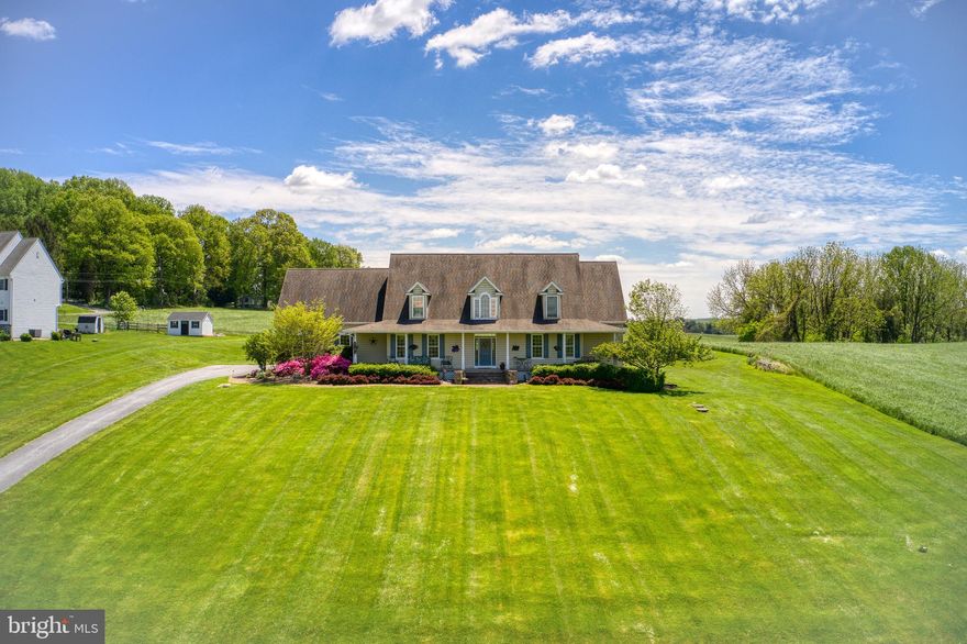 Come see this stunning home, custom built by the owners in 2003.  Filled with beautiful details and homey touches, and settled on a tranquil 2.2 acres of land, once you step through the door you’ll never want to leave. The front porch offers a sweeping view of the surrounding countryside and a quiet, shady place for you to sit with a glass of lemonade and your favorite podcast. Then step inside the grand entryway to find hardwood floors, light-filled windows, and vaulted ceilings. To the left is a formal dining room with tall windows and easy access to the kitchen. You’ll never think twice about hosting Thanksgiving dinner again.
The kitchen provides acreage of cherry cabinetry, European porcelain tile floors, and a sprawling island. A breakfast nook overlooks the back garden with lovely glass doors that open onto the back porch – still more space for entertaining, and grilling out. The kitchen opens to the living room with 19-foot ceilings, gas fireplace, and floods of natural light.  Also on the first floor is the primary bedroom suite. Broad windows, a walk-in closet, and ensuite bathroom create the ultimate retreat.   An additional bedroom on the main floor, with a generous walk-in closet, can be used as a guest room, den, or office. Finally, a half bath and convenient laundry room completes the amenities on the main floor.  Up the grand staircase you’ll find two more expansive bedrooms and a full bathroom. Each bedroom has a walk-in closet, gabled windows, and new plush carpet.  Connecting the 2nd floor rooms is a loft-like hall that overlooks the airy living room and out onto the backyard.  The expansive basement is an open canvas for a family room, play room, crafting space, or wood shop. Above the 2-car garage is a bonus room that can be transformed into an additional bedroom suite, guest quarters, or home office. Move-in-ready and with space to grow: this home has everything. Surrounded by roiling countryside, this Nottingham home is one you don’t want to miss.