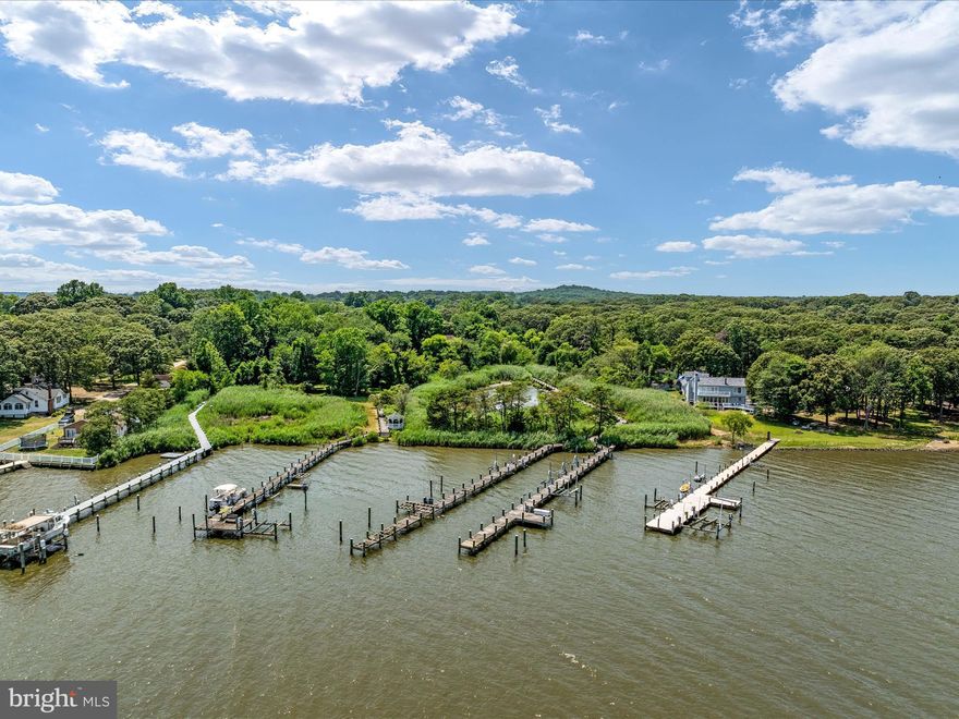 This luxurious mid-century modern home is the perfect all-seasons waterfront retreat nestled on nearly 2 acres of abundant land, boasting over 3900 square feet of unparalleled living space. Located on Sillery Bay and the Magothy River, this residence offers privacy and tranquility, with a prime position just steps from a fabulous pier and breathtaking views from the pier.  The modern architectural design blends seamlessly with its natural surroundings and is complemented by significant amounts of natural stone in both the exterior and interior. The entrance has attractive slate steps to double doors. Enter into expansive two story spaces and the striking view of a magnificent central, two-story living room with a wall of windows overlooking the substantial outdoor living areas and the wooded surrounding yard. The step down living room has a two story, full stone hearth, wood burning fireplace. The adjacent dining area and kitchen are divided by a two sided, stone hearth, gas fireplace. A spacious dedicated workspace on the main level has sliders to the composite deck with another two sided, stone fireplace overlooking the lap and lounge pool. The main level primary room with a corner gas fireplace and cathedral ceiling, has a large walk-in closet, 2nd large closet and an ensuite full bath with jetted soaking tub and 96" vanity. A connecting door provides a 2nd full bath on the main level with hallway access and includes a walk-in shower and 72" vanity. The upper level gallery overlooks the central living space and two story entry rooms. There are 3-4 additional spacious bedrooms and 2 additional full bathrooms on the upper level. The composite deck adorned with natural stone pillars between the baluster and rail system has a covered entertainment area with a wet-bar, built-in JennAir grill with Barbeque Galore side burners, granite countertops and Thermador range vent. Enjoy a short stroll on a path to the shared boardwalk with tranquil views of a tidal pond on the adjacent property, opening to the left side, privately owned 102' of water frontage, pier with 2 slips, one with a boat lift and 3 personal watercraft lifts. Clean the catch of the day on the pier's cleaning station while taking in the breathtaking views of Sillery Bay and Gibson Island. An attached 3-car garage and a detached 1-car garage provide ample vehicle storage in addition to multiple carports in the mid century modern style. This beloved haven offers the best of both worlds – a private wooded retreat with direct access to a fabulous pier and stunning water views, all conveniently located near commuter routes to DC, Baltimore and Annapolis, BWI airport, & recreational activities, ensuring every convenience is within reach. Don't miss this opportunity! Schedule your private tour today!