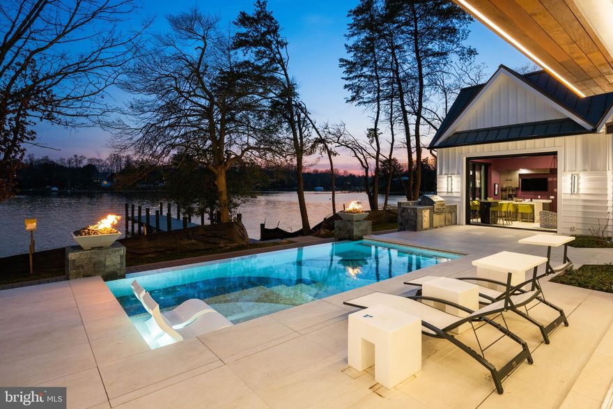 Set on a remarkable peninsula of land along Lake Ogleton, with water embracing the property on three sides and direct access to the Chesapeake Bay, this newly constructed waterfront residence is a masterclass in modern design and craftsmanship. From the moment you enter, the home reveals itself through soaring ceilings, dramatic walls of glass, exceptional design and uninterrupted water views that create a seamless connection between architecture and setting.

Every space has been thoughtfully curated to balance bold contemporary style with effortless livability. The expansive open floor plan is anchored by a striking gourmet kitchen with 2 oversized stone islands, custom cabinetry, and top-tier appliances, flowing seamlessly into the family room and waterside entertaining areas, perfectly designed for both intimate moments and large-scale gatherings. A showstopping, glass-enclosed, temperature-controlled wine wall is thoughtfully positioned between the living and dining rooms, creating a dramatic focal point. Framed by views of the stunning saltwater pool and sparkling waterfront beyond, it serves as both a refined display and an elegant backdrop for entertaining.

The main-level primary suite is a true retreat, positioned to capture the surrounding water from multiple exposures and offering the rare luxury of dual spa-inspired baths and two custom walk-in closets. Upstairs, three beautifully designed ensuite bedrooms provide exceptional accommodations, complemented by an additional flexible living space with private balcony overlooking the water.  All accentuating the home’s emphasis on light, volume, and views.

Outdoor living unfolds as a private resort. A waterside pool with heating and chilling capabilities, outdoor kitchen,  and expansive stone pool deck create the ideal setting for sun-filled days and evenings by the water, while the thoughtfully designed cabana/lounge, with a guest suite above, offers a sophisticated extension of the home for visitors. The property’s unique point of land setting enhances both privacy and perspective, with panoramic vistas in every direction leading down to the private deep-water pier and effortless access to the open Bay.

Just minutes from downtown Annapolis and convenient to major commuting routes, this is a rare opportunity to experience a level of waterfront living where architectural precision, elevated finishes, and an extraordinary setting converge into something truly exceptional. Welcome Home!