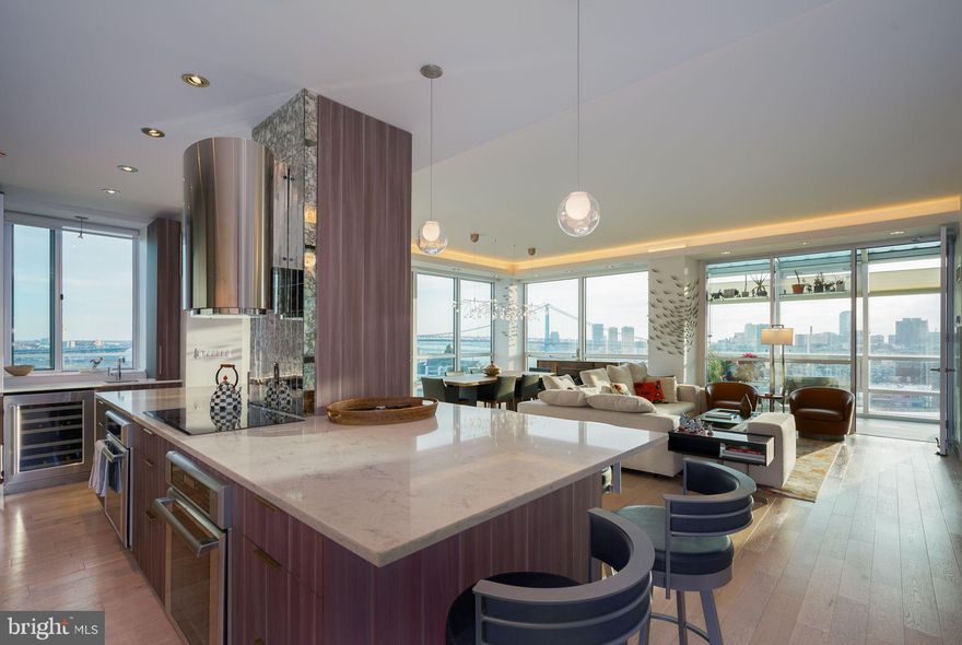 No expense has been spared in this Southeast corner MINI-PENTHOUSE unit in The Peninsula at Waterfront Square Condominium & Spa, on the resale market for the first time!  Inclusive of TWO parking licenses and same floor STORAGE UNIT, this 2,349 sq ft mini-penthouse consists of 3 bedrooms, 3.5 bathrooms, a SOLARIUM, laundry room, and almost a 500 sq ft private terrace for entertaining!  P1402 showcases panoramic, unobstructed views of the Delaware River, Ben Franklin Bridge, and Center City Skyline through oversized floor-to-ceiling windows.  This mini-penthouse recently underwent a half million-dollar renovation.  
Upon entering this fully open concept floor plan, one will notice they are in an ample size foyer with half bath situated here, as well as a hidden walk-in coat closet/pantry combo for convenience.  Moving further into the unit, step into the heart of culinary excellence with this extraordinary 13-foot kitchen island, meticulously designed to elevate your cooking experience to new heights. Crafted with both functionality and aesthetics in mind, this expansive Cream Granite island seamlessly blends style with practicality, offering an abundance of storage space.  Embedded within the island are a plethora of cabinets (16, to be exact), integrated to maximize storage efficiency without compromising on style.  The periphery Granite is White, and the perimeter cabinet total is an additional 18, with some cabinets soaring as high as 68'' tall, built around natural stone tile and under-shelf lighting.  There is a Coffee bar behind an Aluminum vertical pocket door, adjacent to a wet sink, on the East wing of the kitchen.  The appliance package consists of Thermador double built in ovens, induction cooktop with range hood, panel dishwasher, massive French door refrigerator, built in Microwave and Wine r the kitchen, there is a laundry room with full size Washer and Dryer, as well as utility sink and additional storage, hidden behind a pocket door.
Of course this mini-penthouse has a built-in Sonos audio system, as it was meant to entertain.  Beautiful pendant, recessed and tray ceiling lighting showcases different seating areas throughout the unit, inclusive of a double Heracleum chandelier over the dining area. The 5% translucent motorized shades offer the perfect balance of privacy and natural light, filtering sunlight to create a soft, diffused ambiance throughout the space.  The 3 bedrooms have blackout shades in addition to the translucent shades.  The guest room has painted solid Maple Dovetailed drawers, and the office built-ins are finished in Cherry stain.  The primary bedroom has soft closed slides, incorporated with glass overlay, done in brushed Alumina color.  There are 3 different climate zones throughout P1402.The mini-penthouse features wide plank Oak hardwood flooring throughout the living spaces, and marble tile in the bathrooms.  The primary bathroom is the ultimate in relaxation and luxury, designed to indulge your senses and elevate your daily routine. Featuring a built-in vanity area, a state-of-the-art Suntouch radiant heat system in the shower, and the pièce de résistance – the Duravit 6-foot-2-inch freestanding bathtub.
Waterfront Square Condominium & Spa is a premier gated community offering 24/7 guard and gate, as well as concierge, pool and hot tub with river deck, fitness center, sauna and steam room, massage rooms and community rooms.  There is a 3- level garage, with Philadelphia's largest green roof situated on top.  Waterfront Square resides on  a 9.5-acre riverfront enclave, with lush manicured outdoor common parks and gardens right on the river's edge.  Management is on site, and Waterfront boasts an advanced security system with closed-circuit television.  Global Limousine runs on site M-F, taking residents as far as 30th street and back home to their gated community.  The river deck is oversized, encompassing a 25-meter heated lap pool (junior Olympic).