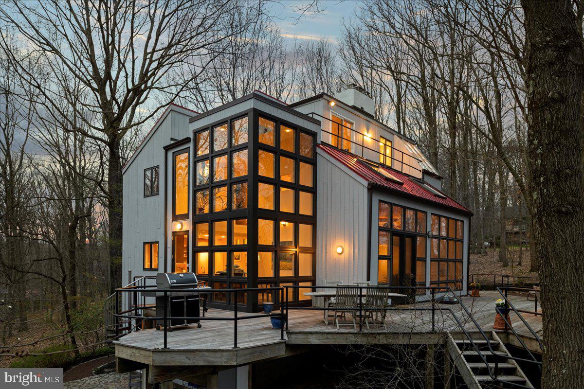 This remarkable custom architectural masterpiece rests atop a tranquil, wooded hillside accessible via one of Bucks County's most picturesque roads. With its floor-to-ceiling windows, open layout, expansive glass walls, and incorporation of natural materials and hues, this contemporary home seamlessly integrates the outdoors with the indoor spaces. Enjoy the stunning fireplace from all three levels, including a double-sided fireplace on the main level highlighting the living room and dining room. The large family room is perfect for weeknight lounging and entertaining large groups on weekends. A unique and custom office is tucked away beyond the dining room with plenty of bookcases and storage. The kitchen opens to a breakfast nook where you can enjoy a cup of coffee while admiring your secluded woodland estate. On the second level, you’ll find two bedrooms, a generously sized bathroom, a family room and desk space, beautiful hardwood floors, vaulted ceilings, and a balcony with a view of your grounds. The primary bedroom encompasses the entire third level, providing a private space for rest and relaxation. Accentuating the suite, a deck offering a canopy view of the pool is an ideal spot for enjoying all seasons. Invite your guests for extended stays, as this home also features a ground level suite with a bedroom, full bathroom, breakfast area with a wet bar and island, and a living room that opens to a paver patio. This home will surprise you with the many thoughtful custom features throughout each level. The laundry and a two car garage are accessed on the ground level. Embrace outdoor entertaining on the three-acre property, boasting a stunning heated lap pool, waterfall and spa, along with extensive decking overlooking the pool. This residence enjoys a convenient location nestled between New Hope and Doylestown, offering effortless connections to New Jersey, New York and Philadelphia and is located in the Blue Ribbon Central Bucks School District. This home provides complete privacy and is a must see in person home!