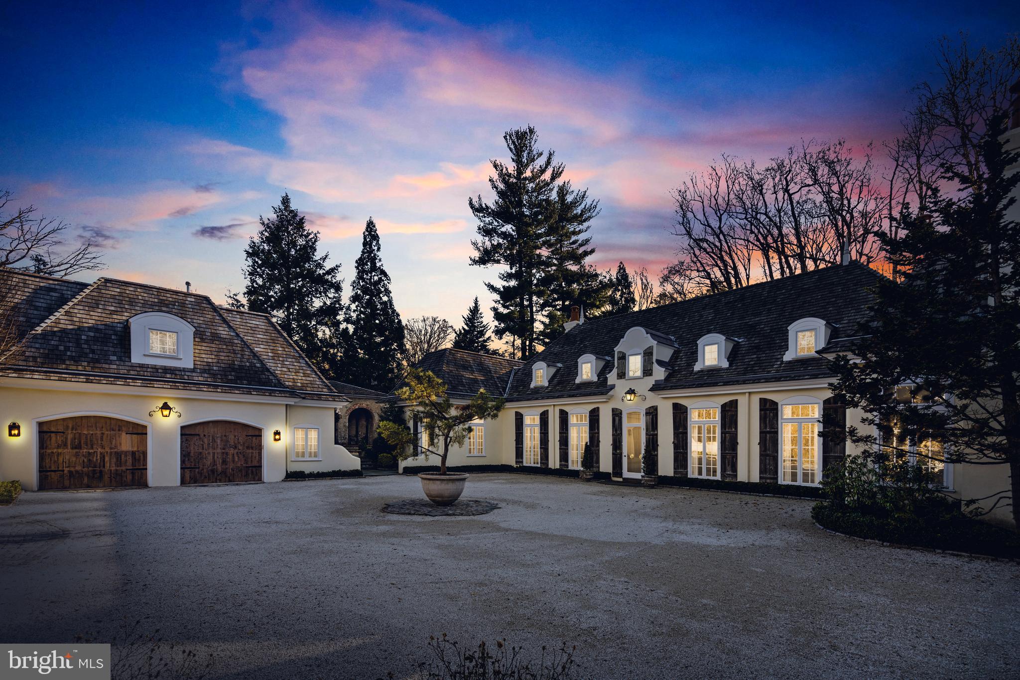 Welcome to 500 Rose Lane, located in the serene and picturesque Haverford Lower Merion Township. Situated on a sprawling 3-acre parcel of land, this magnificent home offers the perfect blend of privacy and luxury. As you approach the property, a winding drive leads you to a gravel courtyard, surrounded by meticulously maintained gardens.
The country French exterior of the home exudes charm, with rustic wood shutters and a cedar shake roof adding to its character. Step inside, and you'll be greeted by a grand entrance foyer with soaring 15-foot ceilings, adorned with floor-to-ceiling windows that flood the space with natural light. The transverse foyer seamlessly connects the various areas of the home.
The main living area is a testament to open concept design, encompassing a spacious dining room, living room, and library. Anchored by fireplaces on either end, this expansive area offers a warm and inviting atmosphere for gatherings and relaxation.
The sparkling white kitchen is a chef's dream, featuring slab marble counters, tall display and storage cabinetry, and top-of-the-line appliances. Adjacent to the kitchen is a cozy fireside family room and an octagonal breakfast room, providing a tranquil setting for casual meals and morning coffee.
The primary bedroom, conveniently located on the first level, is a true retreat. It boasts a generous sleeping room with its own fireplace, two ensuite baths, and multiple reach-in or walk-in closets. Connected to the primary bedroom is an intimate den/family room, also with a fireplace, which could easily be repurposed as an additional bedroom if desired.
One of the highlights of this home is its breathtaking views of the gardens from the main living area. Western-facing windows frame the lush greenery, creating a serene backdrop for everyday living. Step outside onto the expansive blue stone terrace, where you can bask in the beauty of the surroundings or take a refreshing dip in the inviting pool.
Upstairs, you'll find two generously sized guest suites, each with its own private marble bath and ample closet storage. These suites are ideal for accommodating guests for long-term stays, ensuring their comfort and privacy.
For added convenience, there is a separate suite located above the 2/3 car detached garage. This versatile space boasts high ceilings, a small wet bar with refrigeration, a large bedroom, a living area, and an attached bath.
In addition to its many features, the remarkable home at 500 Rose Lane boasts a captivating open-air covered stone loggia, reminiscent of the architecture found in the original estate. This enchanting space is accessible from both the courtyard and the rear and side gardens, further enhancing the seamless connection between indoor and outdoor living.
The stone loggia exudes elegance with its arches, creating a striking visual element and adding a touch of sophistication to the home. This inviting space serves as an exquisite entertaining area, perfect for hosting gatherings or simply relaxing while enjoying the beauty of the surrounding gardens.
Whether you choose to gather with friends for an evening cocktail party, savor a delightful al fresco meal, or simply unwind with a good book while surrounded by nature, the open-air covered stone loggia provides a versatile and captivating setting for memorable moments.
Immerse yourself in the enchanting ambiance of this elegant entertaining area, where the timeless charm of the original estate is seamlessly blended with modern luxury, making it a truly exceptional feature of 500 Rose Lane.