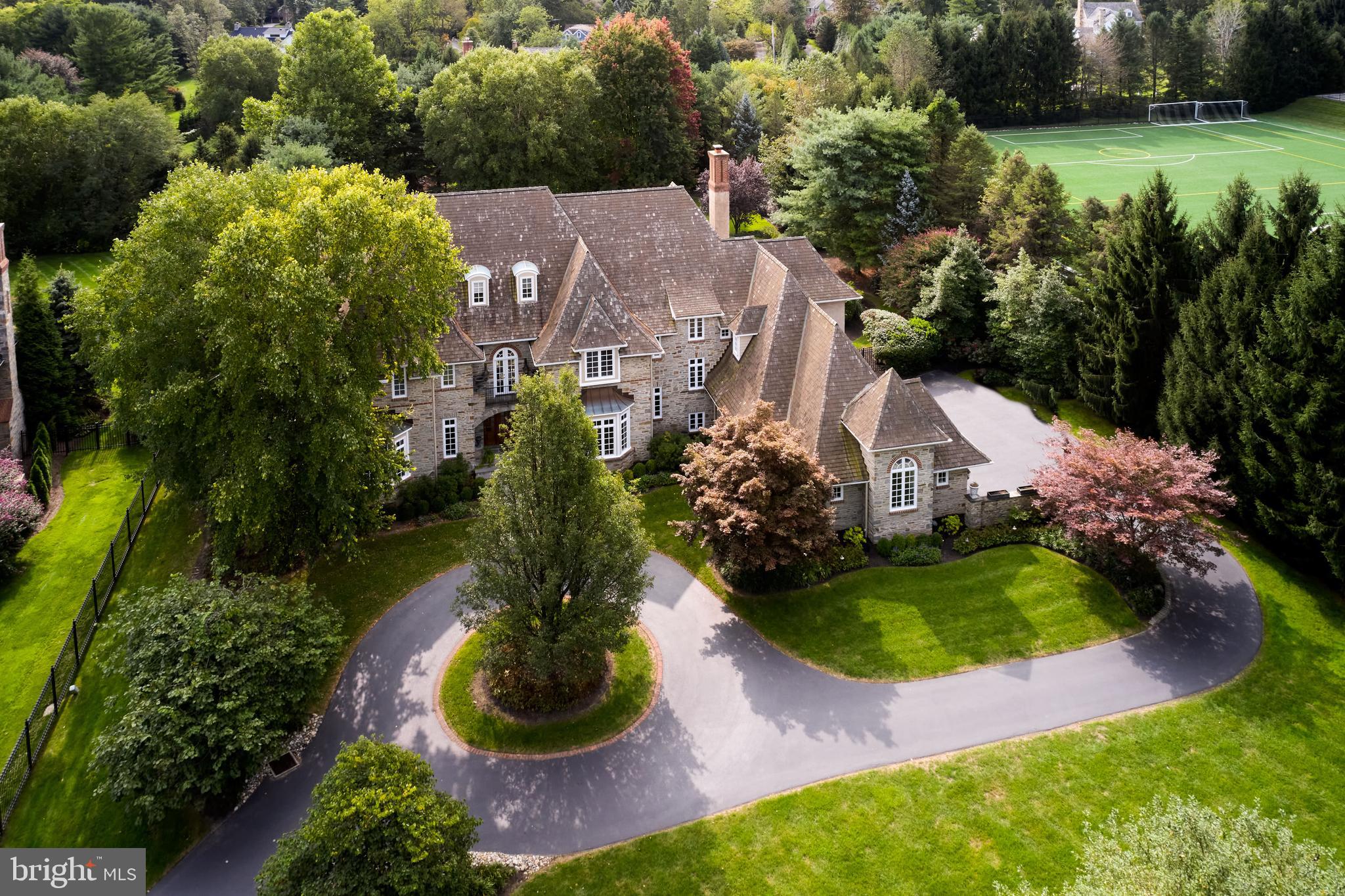 Sophisticated stone and brick detailed manor home positioned on a lush 1.4 acre parcel, ringed by mature landscaping for privacy by the pool and hot-tub is enlivened by perennial color and low maintenance, irrigated gardens. Wide stone stairs lead to a glass paned mahogany entry door and beyond to a spacious entrance hall designed to seamlessly connect the Center foyer floor plan yet large and inviting enough to be a space capable of both service and entertaining. Rich, character grade hardwood floors span the first level, and are balanced by multi-piece crown moulding, paneled wainscoting and intricate ceiling detail. To the left of foyer find the formal LR with fireplace and inset piano bay. The formal powder room is tucked between the LR and a handsome fully paneled library which is warmed by a gas burning fireplace and highlighted by walls custom shelving and bay window. An outfitted stone topped service bar connects the reception foyer to the library. To the right of entry an elegant dining room flows through a furniture quality Butlers pantry into an open kitchen with exceptional ceiling height, superior flat prep and storage space, oversized seated island and extraordinary light which flows from the glass surround Keeping Room, separate vaulted ceiling Breakfast Room and beyond into a large Family Room with coffered ceiling and fireplace. French doors from both family and breakfast rooms lead to the flat blue stone terrace, grill and pool. A second home office, styled with wrap around windows overlooks the rear yard and back court yard. Ascend the front stairs to an expansive master suite. Front sitting room with south facing overlook balcony, elegant volume ceiling master bedroom and really well-designed dressing area, spacious separate walk in closets and two-sided bath, (her side with tub) separate water closets and vanities. All other bedrooms on this level flow from a wide, paneled foyer; each enjoy generous closet space and their own bath. A large laundry room with storage complete this level. A finished third floor could be purposed as a 6th Bedroom Suite or office. Fully finished lower level has additional entertaining space with billiard room, custom bar with sink and refrigerator, open tv area and primary storage.