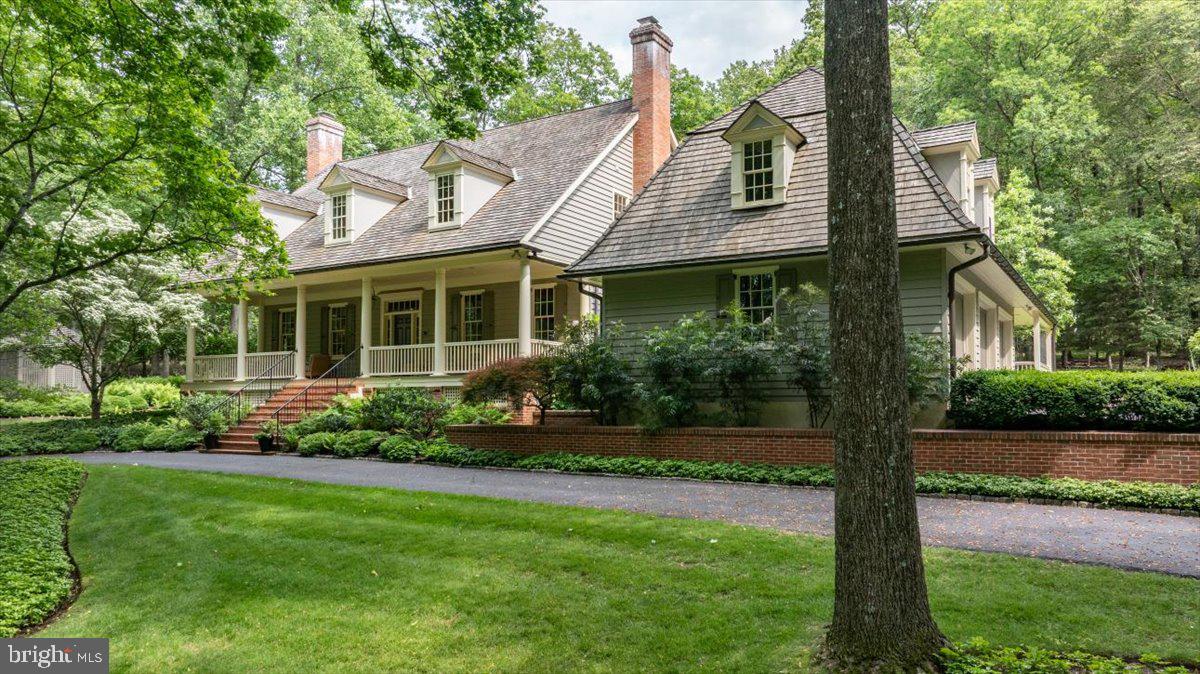 The epitome of refined elegance is presented at 6420 Old Carversville Rd, a sanctuary where tranquility and beauty coexist. This pristine residence is being introduced to the market for the first time, showcasing exemplary architectural design by Lynn Taylor and masterful craftsmanship executed by Jarrett Vaughn.
Ensconced in understated glamour, the home's frontage boasts a covered porch, supported by stalwart columns that frame a welcoming entrance, an idyllic spot for relaxation. The main level is a testament to sophisticated luxury, featuring walnut hardwood flooring, towering ceiling heights, and intricate millwork. The formal parlour emanates style, furnished with bespoke library shelving, a gas fireplace, and an aesthetic reminiscent of Ralph Lauren inspired interiors. The adjacent two-story living room exudes warmth and comfort, filled with natural light from a wall of French glass doors that open to picturesque views of the patio garden and fountain. The gourmet chef's kitchen is outfitted with a recently installed Wolf range cooktop, a bespoke-crafted hood, double ovens, a Sub Zero refrigerator, and a granite-topped center island that is gracefully positioned above radiant heated flooring. This eat-in kitchen is encased by panoramic windows, creating a truly remarkable ambiance for dining. The rear patio, equipped with a retractable awning, allows for effortless entertaining throughout all seasons in a peaceful woodland setting. On more ceremonious occasions, the octagonal dining room is an ideal space for special occasions and features a wall of built-in cabinetry for all of your fine dining accoutrements. Notably, the spacious primary suite is situated on the home's first level, appointed with a luxurious soaking tub, glass shower, and walk-in closet. On the second level, two guest bedrooms share an adjoined bathroom, while further down the corridor lies an additional spacious en-suite bedroom. The fourth bedroom suite offers ideal guest accommodations, with access from the second floor or a private entrance off the driveway—providing a quiet, comfortable, and secluded retreat. The fully finished lower level boasts a temperature-controlled wine and cigar cellar, a mini bar, a gym area, a gaming room, and an abundance of additional storage space. Exquisitely manicured exterior landscaping, a charming cottage garden, a full house generator, copper gutters, cedar shingles, and extensive brick walls complete this impeccable property. The quaint township of Carversville, nestled in the heart of Bucks County, PA, boasts a rich history that harks back to the 1700s and continues to flourish as a coveted residential address. Sitting in proximity to the captivating old mills on the Paunacussing Creek, the recently refurbished Carversville Inn, the renowned Black Bass Hotel, the Lumberville General Store, and a variety of cycling trails offering sensational views of the Delaware River, this location is the epitome of a country retreat. Despite its tranquillity, Carversville is still conveniently located close to all main commuter routes, and proudly sits within the boundaries of the acclaimed New Hope Solebury School District. We cordially invite you to tour this exquisite residence for an intimate glimpse into the embodiment of residential perfection.