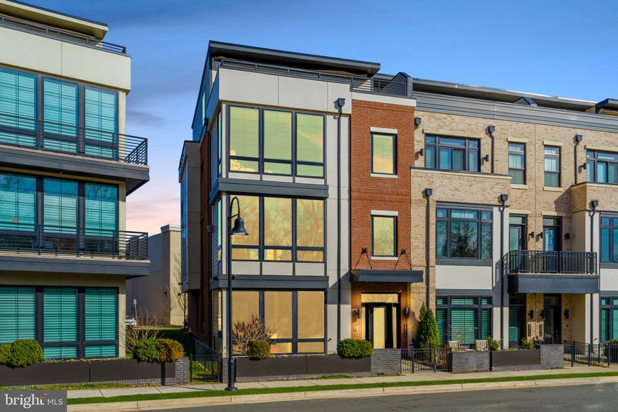 Discover unparalleled luxury in One Loudoun!  Experience resort-style living in this stunning, rarely available, end-unit townhome, with nearly 5,200 square feet of refined space and a private in-home elevator. Overlooking the park's lush greenery and offering breathtaking sunset views, this home delivers a serene escape immersed in vibrant community energy - right at your doorstep.  Impeccably updated and meticulously maintained, it masterfully blends urban sophistication with effortless lock-and-leave convenience.  Ideal for embracing One Loudoun's active lifestyle or enjoying low-maintenance elegance, this residence must be seen in person to appreciate its superior craftsmanship and unbeatable location.  Abundant natural light floods the open, airy layout, making entertaining seamless and everyday living a delight.  Thoughtful design and premium finishes create the privacy and tranquility you crave, elevated by distinctive architectural details that define true luxury.  Highlights Include: 10+ foot ceilings,  private elevator servicing all floors, custom automated window treatments throughout, and advanced smart home automation and security for effortless control.  MAIN LEVEL: A bright, welcoming great room filled with sunlight - perfect as a flexible entertaining space, family hub, or home gym. A separate bonus room with generous closet, full bath featuring a luxury hydrotherapy walk-in tub, and direct garage access complete this level.  LEVEL 2: The entertainer’s heart of the home centers on a chef’s-caliber kitchen with premium Wolf appliances, Sub-Zero refrigeration, custom designer cabinetry, and a massive quartz island. Adjacent sits a spacious area with built-ins, flowing to the rear deck ideal for al fresco dining and grilling. The open-concept design seamlessly connects to the dining area, gracious living room with fireplace and private office - all with park views. A convenient powder room rounds out this floor.  LEVEL 3: Retreat to your serene primary suite framed by floor-to-ceiling windows with custom automated treatments for privacy and sophistication. The spa-inspired primary bath offers dual vanities, a deep soaking tub, and an oversized frameless walk-in shower. An expansive custom walk-in closet provides unparalleled organization. Two additional oversized secondary bedrooms each feature en-suite full baths with frameless walk-in showers and large closets. An upgraded laundry room with built-in cabinetry, sink and linen storage is conveniently located here as well.  LEVEL 4: A versatile bonus room overlooks the private rooftop terrace, paired with a generous bedroom and full bath - perfect for guests or multigenerational living.  The HIGHLIGHT  is your exclusive rooftop terrace - equipped with gas fire-pit for cozy evenings, retractable (and lighted) awning for shaded relaxation, and panoramic sunset vistas over the surrounding green space.  PREMIUM EXTRAS: EV car charger - Comprehensive smart home automation - Ultra-guard security system - Probiotic and electronic air filtration - Whole-home water filtration - Towel warmers - ELFA System built-ins!  AMENITIES: The Club at One Loudoun features meeting rooms, entertainment spaces with catering kitchen, half-court basketball, outdoor pool (with toddler area), tennis and pickleball courts, sand volleyball, dog park, and playgrounds. The Barn hosts year-round concerts, events, and gatherings in its amphitheater.  UNBEATABLE LOCATION: Directly across from the park's growing trail system and scenic pond, and just one block to premier shopping, dining, entertainment, farmers markets, and everyday conveniences. Quick access to major highways, Dulles International Airport, and the DC metro area.  This is more than a home - it's an exceptional lifestyle blending urban vibrancy with suburban charm. If you've been searching for the perfect fusion of luxury, location, and low-maintenance living, your search ends here.