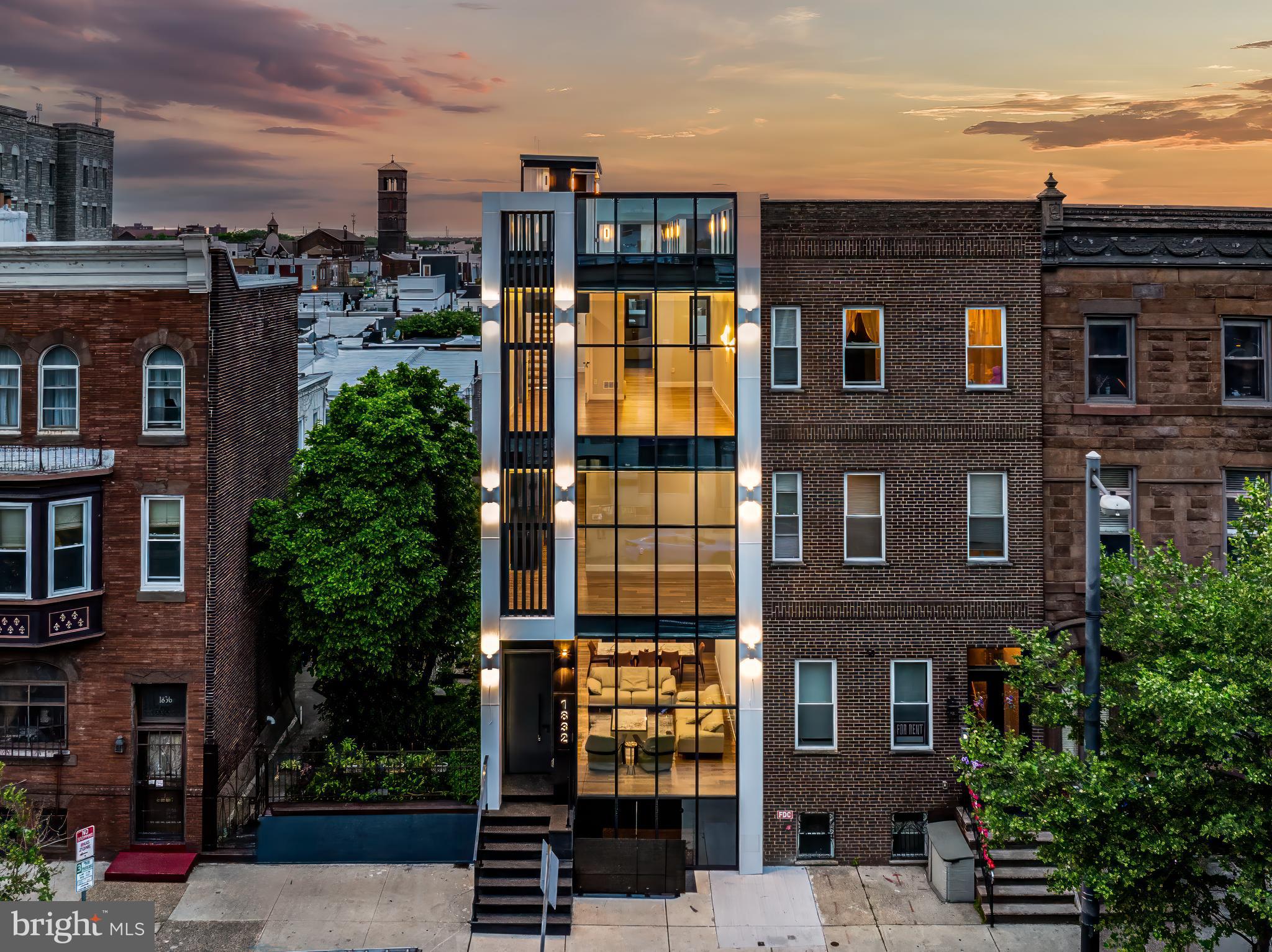 Step into a show-stopping display of sophistication and craftsmanship with this brand new 3-story urban mansion in Philadelphia. This magnificent residence offers unparalleled luxury with breathtaking views of the city. The home features 4,300 sq. ft. of chic, city living with 5 bedrooms, 5 full baths (4 of them ensuite), 2 half baths, and grand living spaces flooded with natural light from high-tech floor-to-ceiling windows. Immerse yourself in the epitome of elegance with a fully finished basement with separate entrances and a rooftop deck offering panoramic 360-degree views of the city.
Upon entry, you are welcomed into a sprawling living room with 12-foot ceilings and floor-to-ceiling triple-pane windows. The warm caramel tones of the hardwood floors blend beautifully with the matte black and gold theme throughout. The living room is anchored by a TV and fireplace combo encased in custom millwork quartz-like surround. Just past the living room is the dining area highlighted by a quartz peninsula with wine storage and a beverage refrigerator. The kitchen is remarkably designed with top-of-the-line finishes, including Dekton Quartz countertops, black stainless steel appliances, and European-style floor-to-ceiling cabinets. A cozy half bath and a home office complete this floor. Enjoy fresh air on the lovely patio, perfect for hosting small gatherings.
The glass panel floating stairs add a touch of sophistication as they run from top to bottom in this home. On the 2nd floor, there are three spacious ensuite bedrooms, each equipped with large custom closets and dimmer light switches. Custom lighting throughout highlights stairways, closets, cabinets, mirrors, and ceilings with a soft ambient glow. The laundry room with ample cabinet space is also located on this floor.
The third floor features the luxurious owner’s suite, complete with endless custom closet space and a marvelous ensuite bath. The spa-like bath includes a water closet, dual vanity, large free-standing tub, and a double glass-enclosed shower with double shower heads, all accented with gold touches.
The oversized rooftop deck provides an amazing outdoor oasis. It includes a wet bar and a half bath, offering a perfect space to host friends and family while enjoying stunning city views.
The finished basement includes private entrances, a full bathroom, and can serve as an au pair suite or professional home office. The home features a dual-zone heating and cooling system for efficient temperature control and an installed sprinkler system.
Included with the sale is a 10-year tax abatement, 1 year pre-paid parking, and 1 year builder warranty. The neighborhood boasts an impressive Walk Score of 97, making daily errands effortless, and offers vibrant Passyunk Square nightlife. Indulge in culinary delights with renowned eateries like Pistolas Del Sur, Barcelona Wine Bar, Le Virtu, Bing Bing Dim Sum, and more just a stone's throw away. Come out and take a look at this amazing masterpiece before it is too late!
