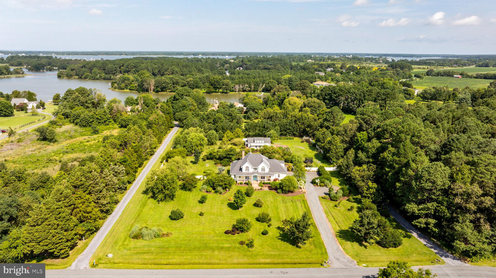 Located in one of the county’s most coveted areas along the Oxford Corridor, this 4-bedroom, 3.5-bathroom custom home offers a spacious layout with a flexible design for modern living. The open floor plan seamlessly connects the kitchen, dining area, and vaulted-ceiling living room with fireplace, creating a functional space ideal for everyday living and entertaining. The updated kitchen features stainless steel appliances, Silestone countertops, an island, and a breakfast nook. Just off the foyer, a private office with French doors provides a quiet workspace, and a formal dining room offers room for gatherings. The main-level primary suite includes two walk-in closets, two vanities, a soaking tub, a walk-in shower, and direct access to the back patio. Upstairs, an en-suite bedroom serves well as a second primary suite, along with two additional bedrooms and a large bonus or recreation room. A cozy sunroom overlooks the elaborate stone patio and outdoor fireplace, offering a peaceful view of the surrounding 2.6± acre property. In addition to the attached 2-car garage, the property includes an oversized detached equipment building—well-suited for boat restoration, woodworking, recreation, or storage. A deeded right of way provides direct water access to Boone Creek, perfect for kayaking or fishing.