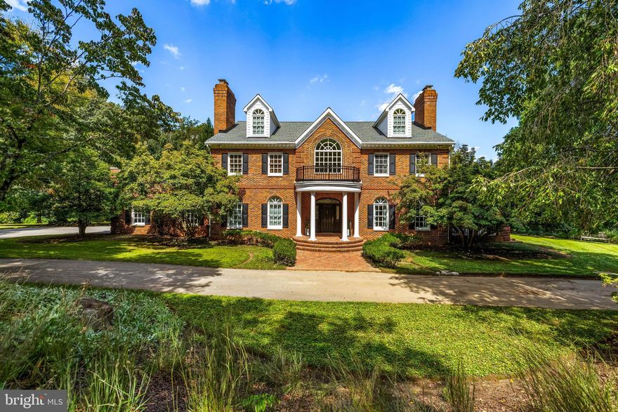 Set within the prestigious Hillstead community of Lutherville, 904 Hillstead Drive is a custom-built Georgian estate offering over 6,500 square feet of elegant, thoughtfully designed living space. With seven bedrooms, five full baths, and two half baths, this stately all-brick home is perfectly situated on a professionally landscaped 2.68 acre lot. Rich architectural detailing, formal and casual living areas, and seamless indoor-outdoor flow create a timeless residence suited for both entertaining and everyday comfort. The main level welcomes guests through a striking two-story foyer accented by black-and-white marble floors, where a semi-circular oak staircase rises beneath a vaulted ceiling. Off the foyer, the living room features hardwood floors, a tray ceiling, and a wood-burning fireplace with a marble mantel believed to be from the H.L. Mencken house. Four sets of French doors open onto a covered porch, extending the living space outdoors. The adjoining formal dining room showcases its own fireplace with a framed brick accent wall, perfect for gatherings both grand and intimate. A butler’s pantry, complete with cherry cabinetry, granite counters, and a glass tile backsplash, connects the dining area to the kitchen. The kitchen is both functional and inviting, featuring cherry cabinetry with custom details, a large island with granite top, and high-end appliances, including Sub-Zero and Thermador. The spacious breakfast area, beneath a coffered ceiling with skylights, opens to a screened porch and a wood deck, creating an ideal setting for casual meals and outdoor dining. Nearby, the richly appointed library offers custom mahogany built-ins, a concealed bar, and elegant finishes. A hall provides flow between the garage, kitchen, and formal spaces, while a main-level powder room off the foyer completes the layout. Upstairs, the second level offers a luxurious primary suite with a fireplace, walk-out access to a private roof deck with hot tub, and a custom-fitted double closet. The en suite bath features a freestanding soaking tub, quartz-topped vanity, rain shower, and beautifully finished tile work. Three additional bedrooms are found on this level, one with a fireplace and custom built-ins, and are supported by a shared bath and a hall bath. A laundry room and walk-out access to a second roof deck round out the floor. The third level offers two more spacious bedrooms, each with walk-in closets, built-in bookcases, and arched dormer windows, as well as a full bath and additional storage. The finished lower level adds flexible living space with a large recreation room, complete with Vermont Castings wood stove and French doors opening to the patio and pool area. A private office, wine room, seventh bedroom with en suite bath, and a half bath provide options for guests, work, and entertaining. The lower level also includes multiple storage areas. Outside, the home is surrounded by mature landscaping, tiered outdoor spaces, and classic hardscaping. A brick walkway leads to the stately front entry, while the rear features multiple covered and open-air entertaining spaces, including a screened porch, expansive deck, and bluestone-bordered patio leading to an in-ground pool with fenced enclosure. With a circular driveway, generous parking, and peaceful privacy, 904 Hillstead Drive offers a rare blend of timeless architecture, modern livability, and gracious acreage in one of Lutherville’s most desirable neighborhoods.