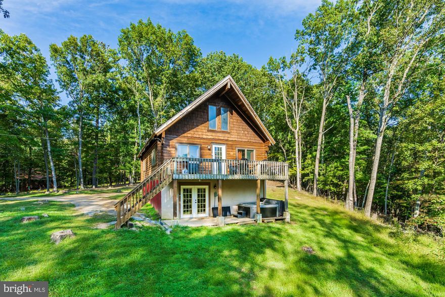 Nestled in WV woods, this large chalet-style cabin offers a unique blend of rustic charm and modern comfort – and is only minutes from downtown Berkeley Springs!  Boasting tall wood-planked ceilings and an abundance of windows, this home invites natural light to fill every corner.  The spacious open loft offers a versatile space, perfect for a reading nook, home office, or extra sleeping area. The updated, modern kitchen is a chef’s dream, featuring stainless steel appliances, a dishwasher, and a spacious island.  With two cozy living areas (on the main floor and a family room in the basement), there's plenty of room to relax, unwind, and enjoy quality time with family and friends. Central AC ensures your comfort year-round, no matter the season.  Outside, you’ll find an expansive deck, fire pit, and a lower deck with a hot tub.  The property also includes access to a community pond just down the road.   The current owner has invested over $77,000 in upgrades. As a vacation rental, this property has been a proven success, generating an impressive $179,000 in rental income over the past 30 months ($52,000 in the past year), and can come with an existing property manager and cleaner.   Hot tub and furniture optional, available for purchase.  See seller docs for a summary of rental history and financials.  $2,000 buyer credit if you continue using the same property manager.  Perfect vacation home or investment property!