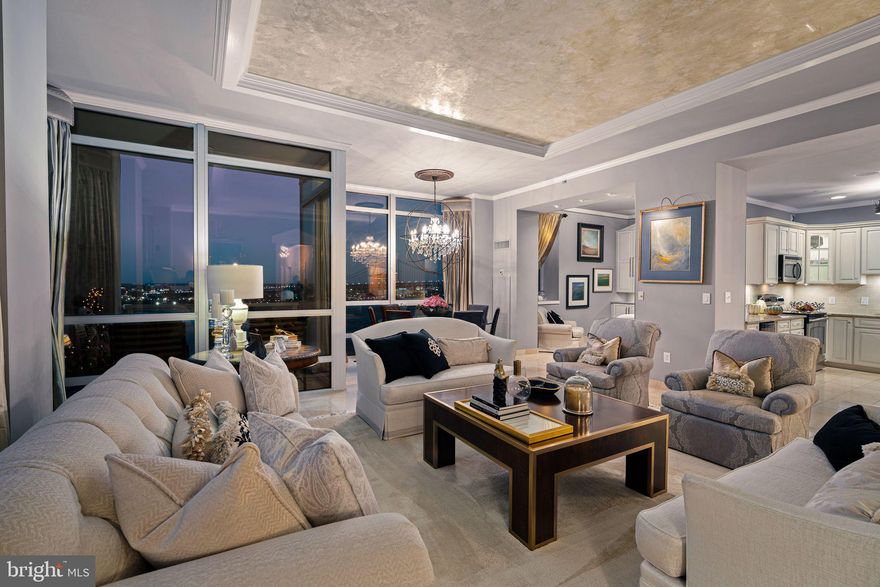 From the moment you step through the doors of P1501, it’s immediately clear this home has been designed with no detail overlooked. A sense of quiet elegance fills the space, beginning in the foyer, where specialty wall finishes shimmer beneath a Schonbek crystal chandelier. The polished marble tile flooring, which continues throughout the residence, sets a tone of refinement, while a double coat closet adds concealed functionality. Just off the entry, the powder room offers a touch of sophistication with its custom vanity, stone countertop, and designer lighting—a perfect welcome for guests.

Heading into the main living area, the home opens to breathtaking scale. Ten-foot ceilings, crown moulding, and floor-to-ceiling windows showcase uninterrupted views of the Delaware River and Ben Franklin Bridge, bathing the interiors in natural light. The coffered ceiling, finished in a Venetian-inspired, hand-painted metallic plaster, captures the glow of day and the shimmer of evening chandeliers. Imported draperies frame the walls of glass.   Suspended above the dining table, a Swarovski crystal orb chandelier becomes a sculptural centerpiece, highlighting this seating area.

Continuing into the kitchen, form and function unite in harmony. Granite countertops contrast beautifully with custom cream cabinetry detailed with glass fronts, complemented by a natural stone backsplash and under-cabinet lighting. A built-in wine refrigerator and full stainless-steel appliance package enhance the space’s practicality, while the open layout encourages both culinary creativity and effortless entertaining. Every element here feels balanced—warm, welcoming, and meticulously crafted.

Beyond the kitchen, the den transitions into an intimate media room, enveloped in sound thanks to the built-in surround system. The polished marble continues underfoot, maintaining visual flow, while layered lighting creates a cozy ambiance ideal for film, music, or quiet evenings in.  The den features custom built-in cabinetry thoughtfully designed to conceal multimedia components, maintaining a clean, streamlined aesthetic. Versatile in function, this space transitions effortlessly between a media room as currently styled, a home office, or an extension of the kitchen for those seeking an open, connected layout.

Stepping through glass doors, the balcony extends the living space outdoors. Here, the river and skyline unfold in full panorama—the bridge’s architectural lines rising gracefully above the water. It’s a peaceful setting that feels miles away from the city below.

A frost panel design, glass door separates the private wing from the entertaining spaces beautifully, while allowing light to filter through.  Each of the three bedrooms offers its own unique vantage and luxurious feel. The primary suite is a private retreat with a spa-inspired en-suite bathroom, walk-in closet, and serene river views. Additional bedrooms ensure ample space for both relaxation and productivity. Every bath is finished with custom tilework, and high-end fixtures, continuing the home’s elevated aesthetic.

Completing the offering are two premium parking licenses and a storage unit, ensuring convenience and peace of mind.  All crystal light fixtures convey.

Waterfront Square Condominium & Spa is Philadelphia’s premier gated waterfront community, offering 24/7 guard and gate security, concierge. Residents enjoy resort-style amenities including an indoor pool and hot tub with river deck, fitness center, sauna and steam rooms, massage suites, and community lounges. The three-level garage supports Philadelphia’s largest green roof, and landscaped gardens across 9.5 acres of manicured riverfront grounds. On-site management and an advanced closed-circuit security system ensure peace of mind, while Global Limousine shuttle service provides weekday transportation to and from 30th Street Station.