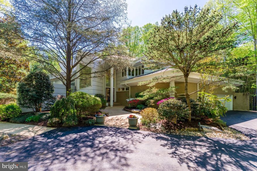 Spectacular does not begin to describe this fabulous residence! Tucked away at the end of a quiet cul-de-sac behind private gates, 9 Oaklyn Court is one of the most striking contemporary residences to come to the market in Potomac this year. Perfectly sited on 2.24 private, level acres with mature landscaping and a resort-style pool, the property offers a serene, parklike setting with exceptional outdoor space and a true sense of seclusion. Designed to impress, the home is filled with natural light, soaring interiors, and captivating views from almost every room. 
A dramatic two-story covered entry introduces expansive living spaces defined by 20+- foot vaulted ceilings, walls of glass, and skylights that flood the home with light. The main level is thoughtfully designed for both grand-scale entertaining and everyday living, with a seamless indoor-outdoor flow. The impressive, step-down living and family rooms are separated by a two-sided gas fireplace, and walls with steps for displaying artwork. The family room has a built-in bar. Each light-filled room has sliding glass doors to the back yard and swimming pool. 
Even the most discerning cook will appreciate the beautiful, renovated kitchen with top-of-the-line appliances, dramatic cabinetry, a center island, built-in buffet, circular designer-glass eating space with stool, and an adjacent eating area that overlooks one of the two large patios, perfect for outdoor eating and barbecuing. Off the kitchen is the dining room with special lighting and floor-to-ceiling windows overlooking the side yard. 
The main level also features the spacious primary suite, a delightful retreat with access to the pool and grounds. The bedroom has a custom wall of built-ins with cabinets, lighted niches, and room for a TV. The adjacent study could also be used as a sitting room, and there are two well-designed large walk-in closets. Two full bathrooms include three separate vanities, a step-up tub, and step-up stall shower. Completing this level are a handsome, cherry-paneled library, two powder rooms, and a large laundry room.
The upper level features four bedrooms, two with en-suite bathrooms and a third full bathroom. The balcony overlook offers an impressive view of the stunning main level.
The light-filled lower level provides a variety of options for informal gatherings. A huge recreation room, lounge with bar area, exercise room, hot tub room and separate bathroom, an additional bedroom with en-suite bathroom, and plenty of storage space complete the interior of this fabulous, approximately 9,900-square-foot house.
The grounds are equally impressive, with a gated, lighted long driveway; beautiful post lanterns; heated pool; expansive patios; and beautifully fenced grounds with room for a future tennis or pickleball court. Ideally located adjacent to Avenel, without the restrictions of an HOA, this exceptional offering combines architectural presence, privacy, and convenience in one of Potomac’s most desirable settings.